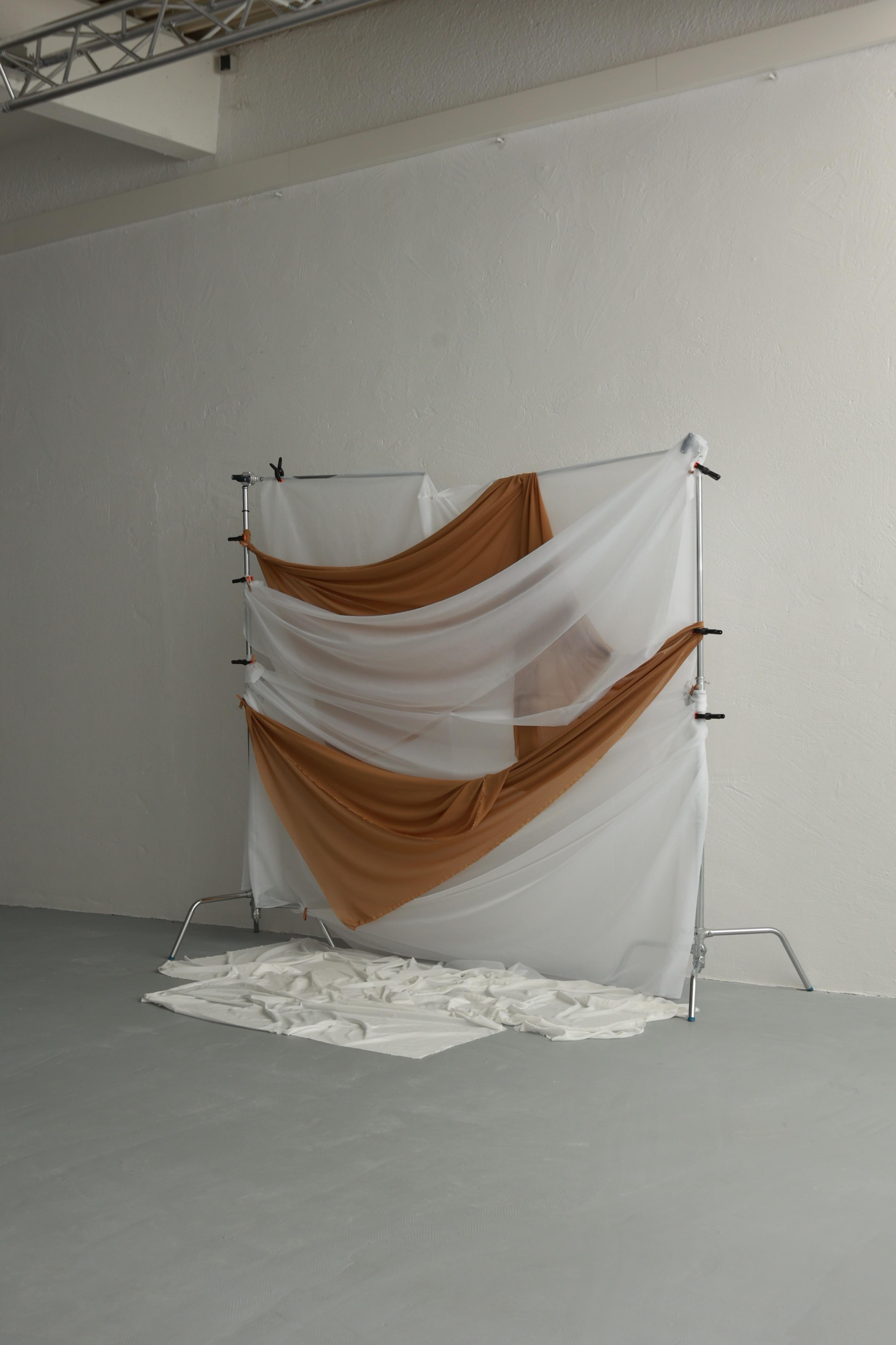 A backdrop made of draped fabric in white and brown is set up against a plain white wall in a spacious room.