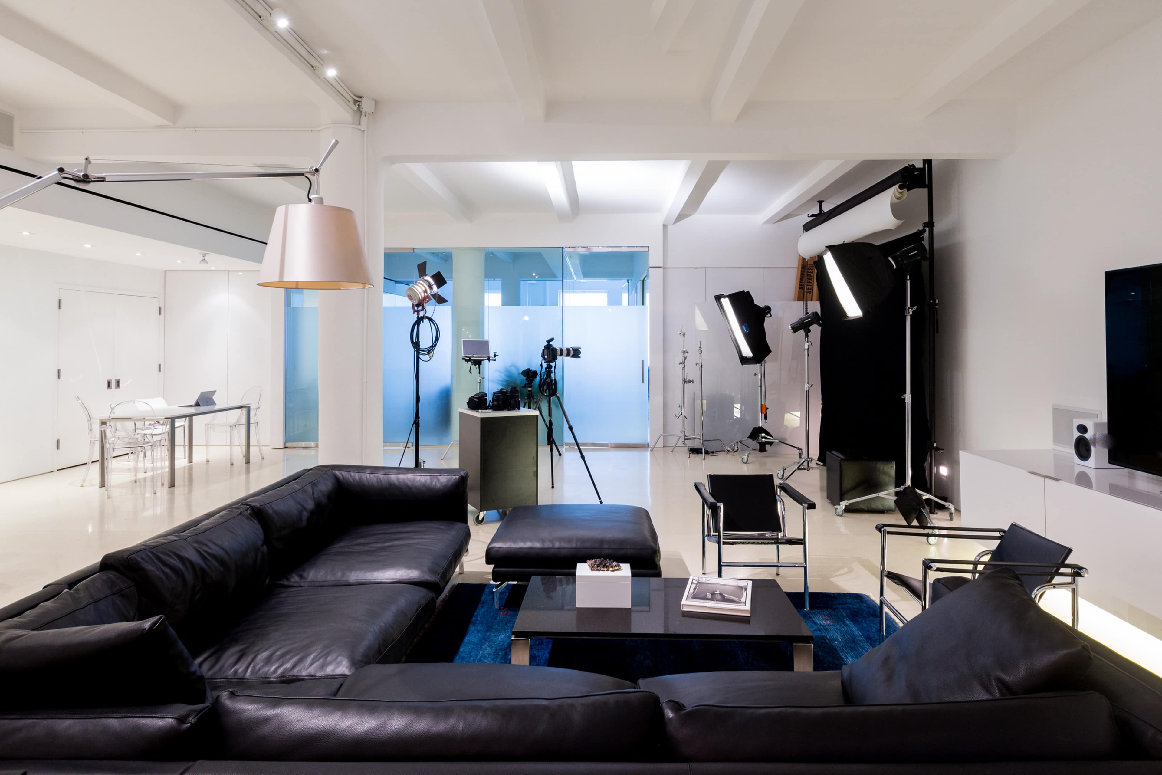 The image showcases a modern living room with a black leather sectional sofa, a coffee table, and photography equipment set up in a well-lit space.