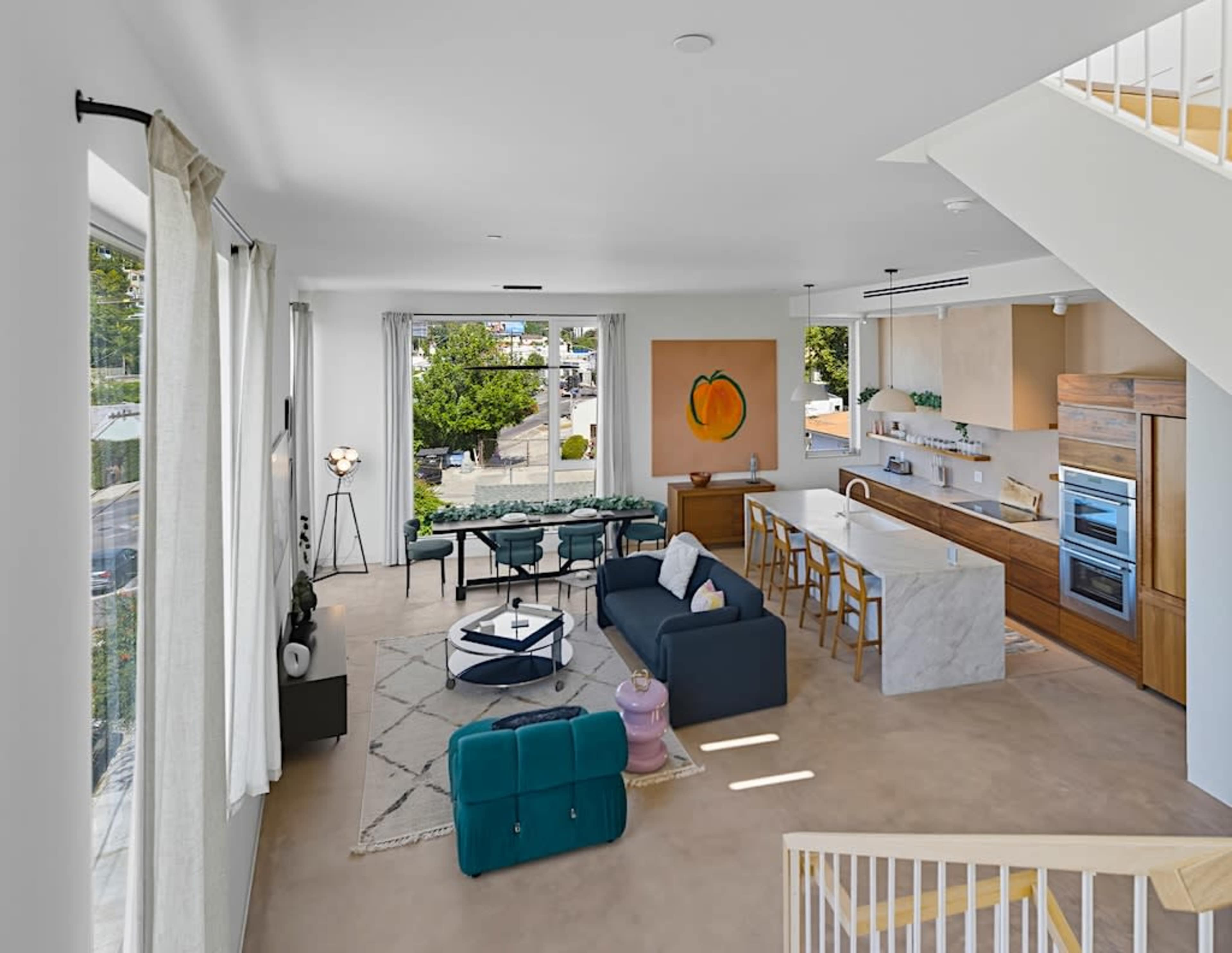 The image shows a modern living space with a blue sofa, a white kitchen island, and large windows allowing natural light to fill the room.