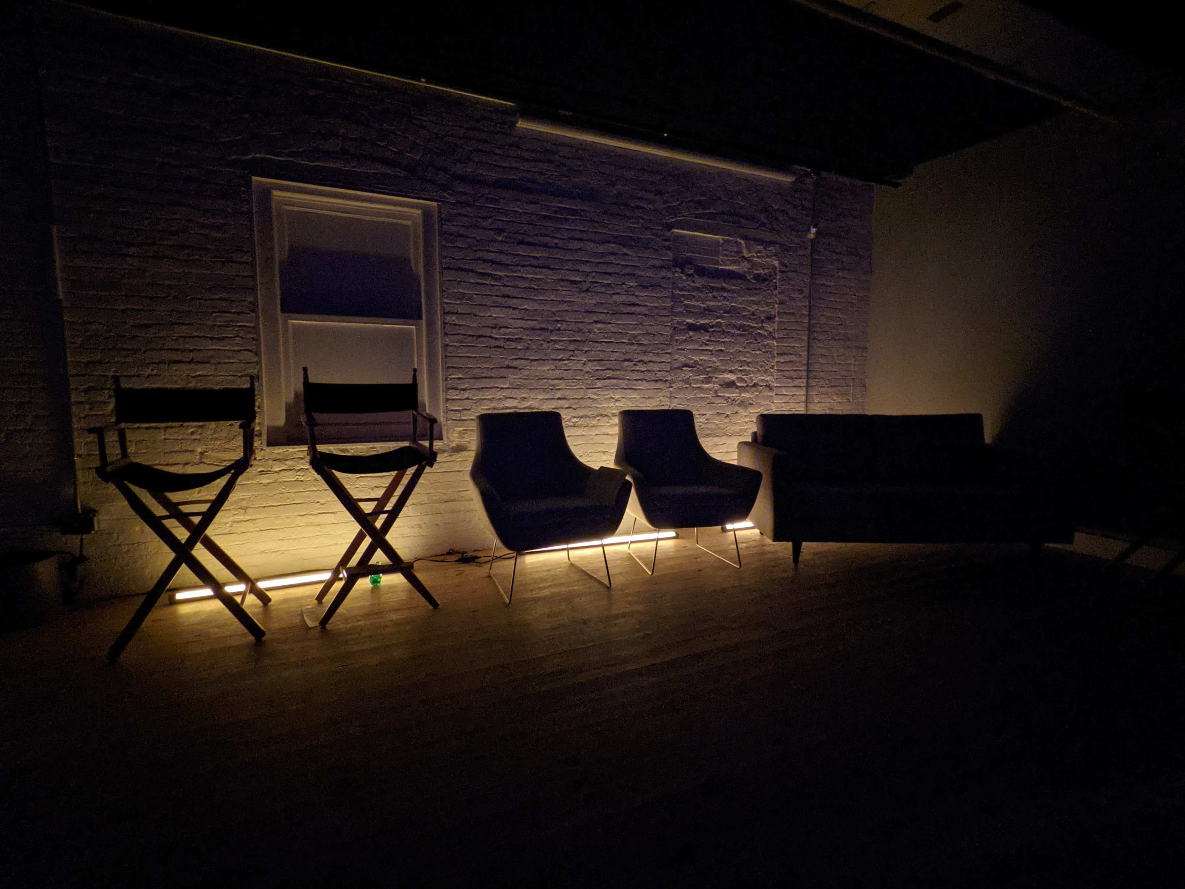 A dimly lit room with three distinct seating options: two armchairs, a sofa, and two director's chairs.