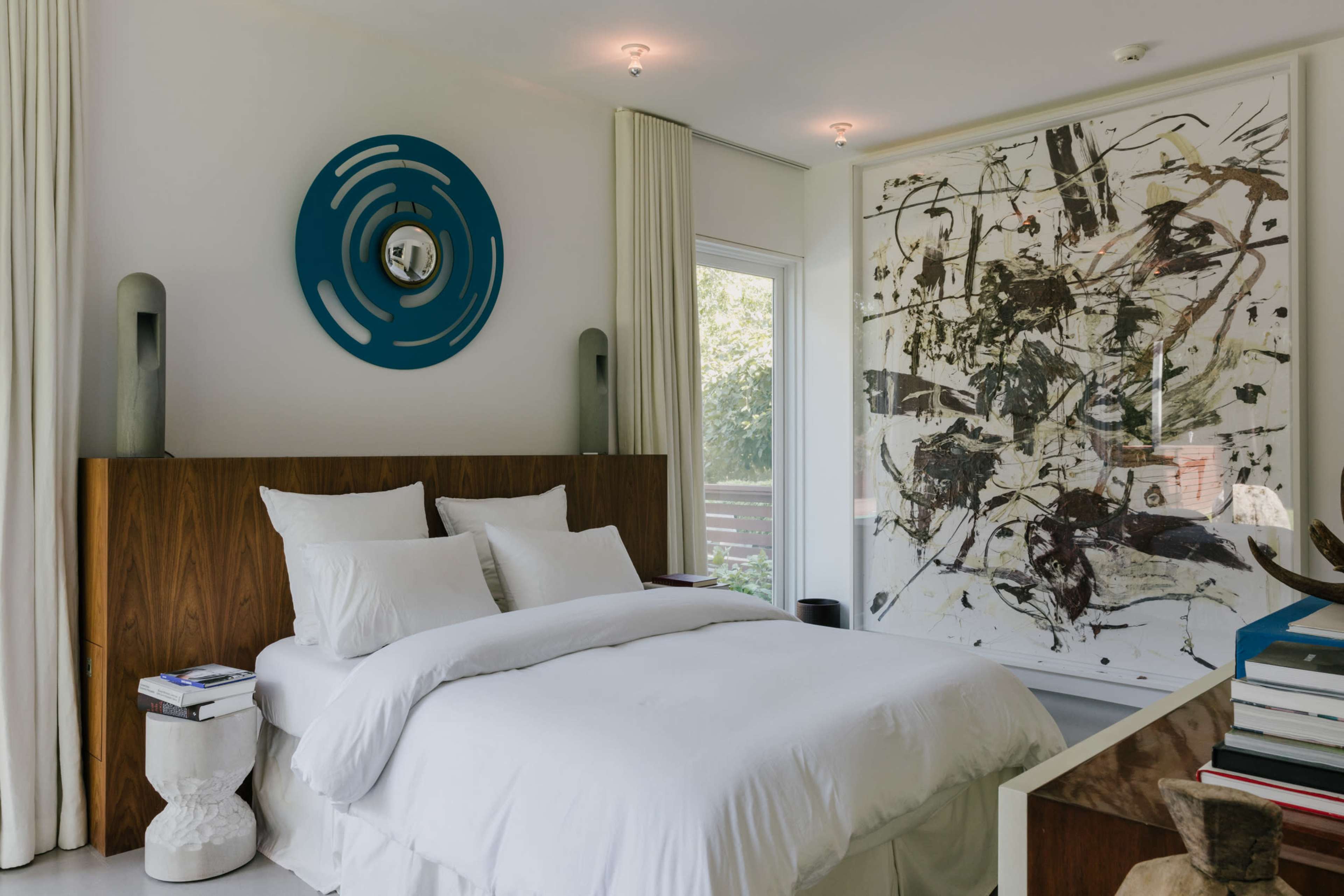 A modern bedroom with a large abstract painting, a wooden headboard, and a white bedding set.
