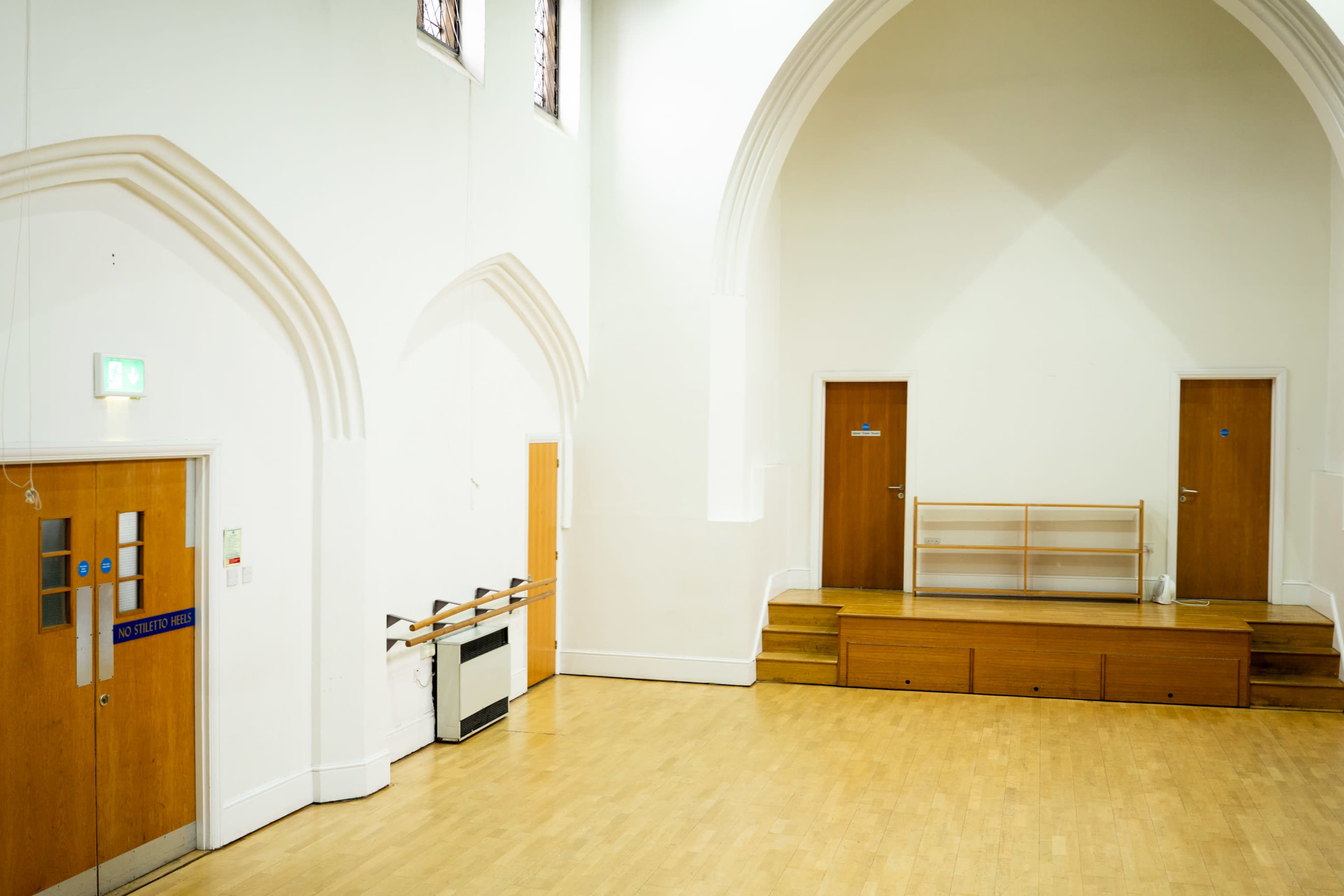 The image shows a spacious, empty interior of a hall with wooden staircases and two doors on one side.