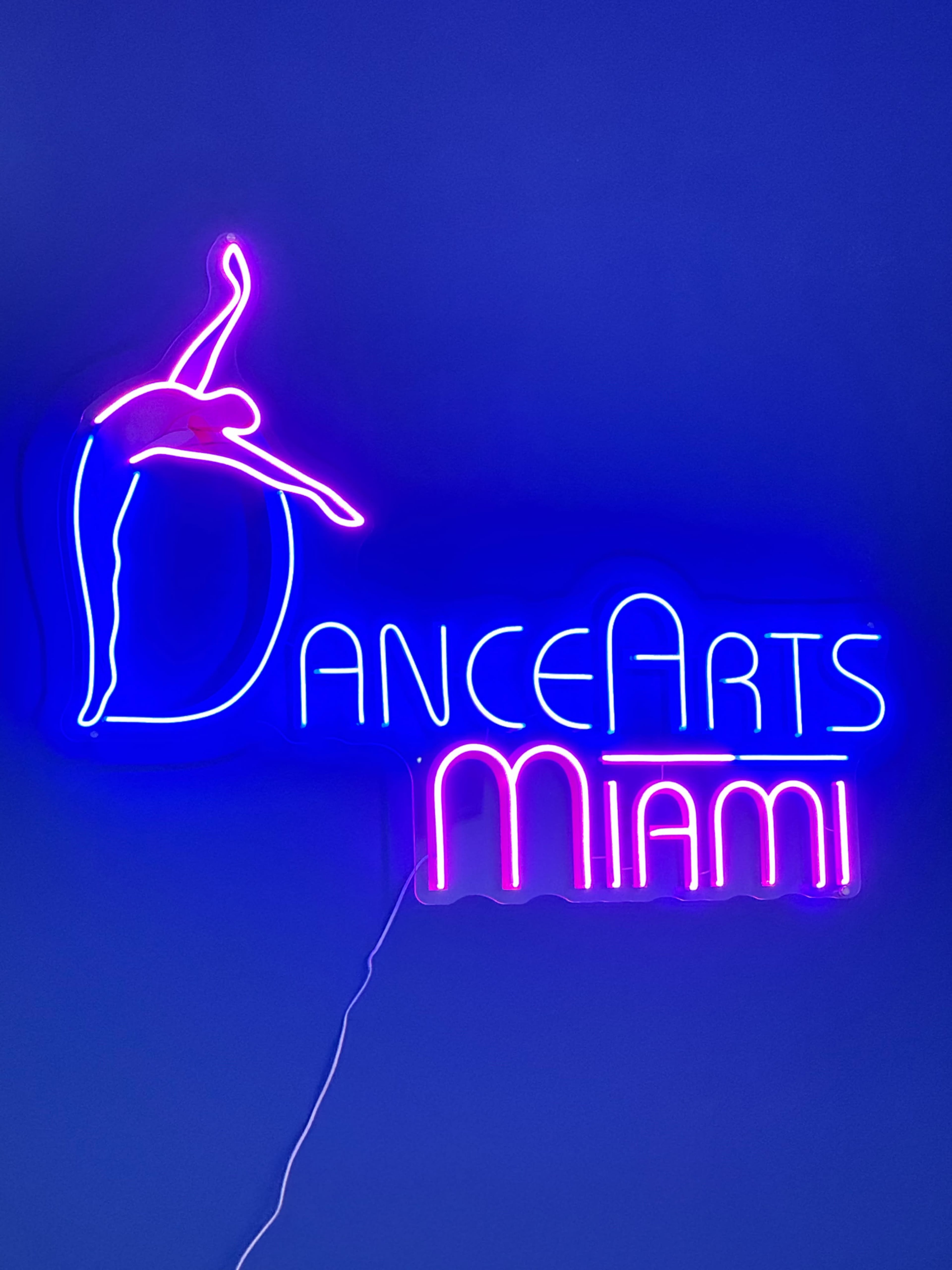 A neon sign displays the text "DanceArts Miami" against a blue background, featuring a dancer silhouette.