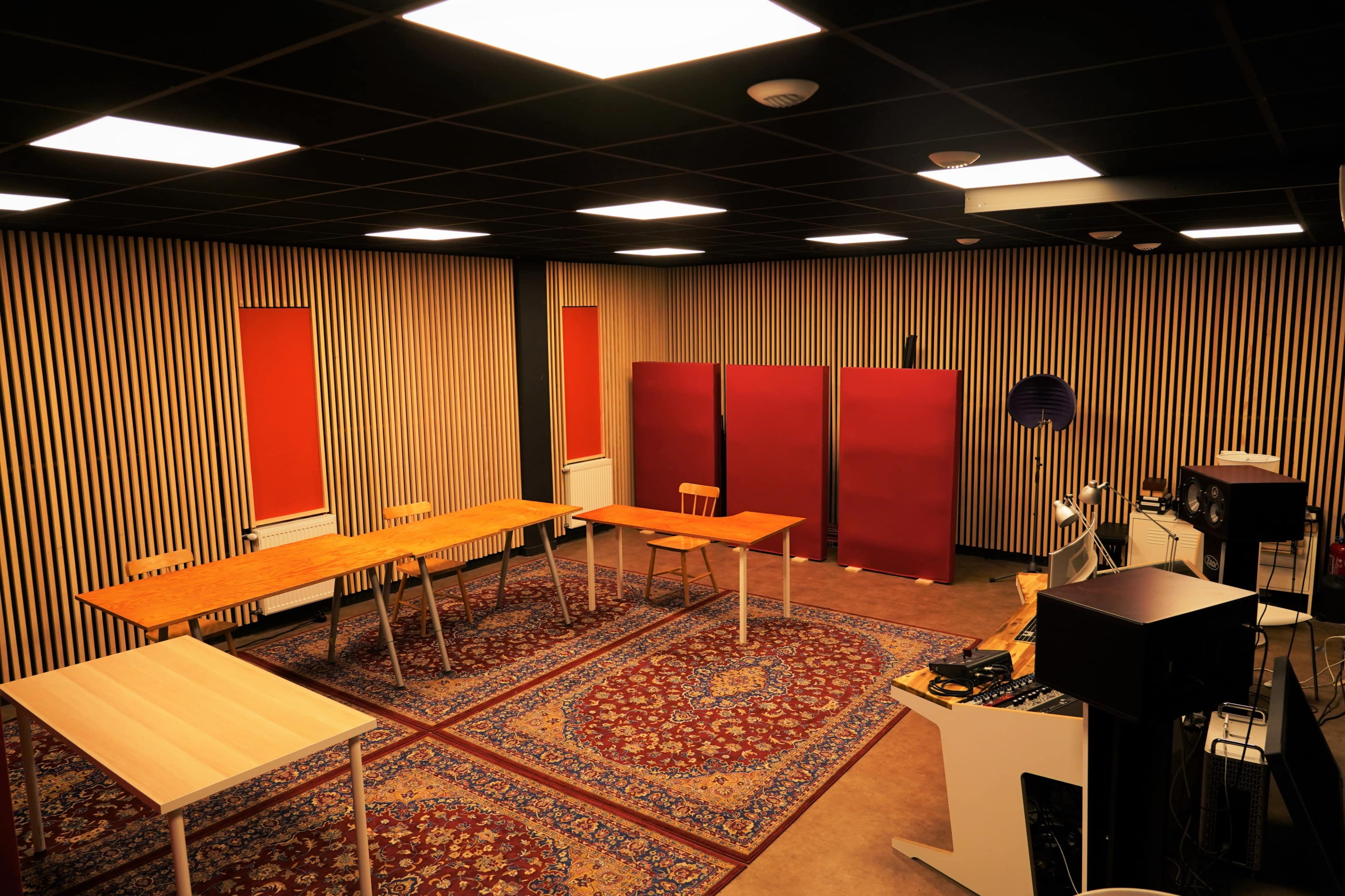 The image shows a room with several wooden tables arranged on a patterned rug, flanked by red window coverings and divided by red partitions.