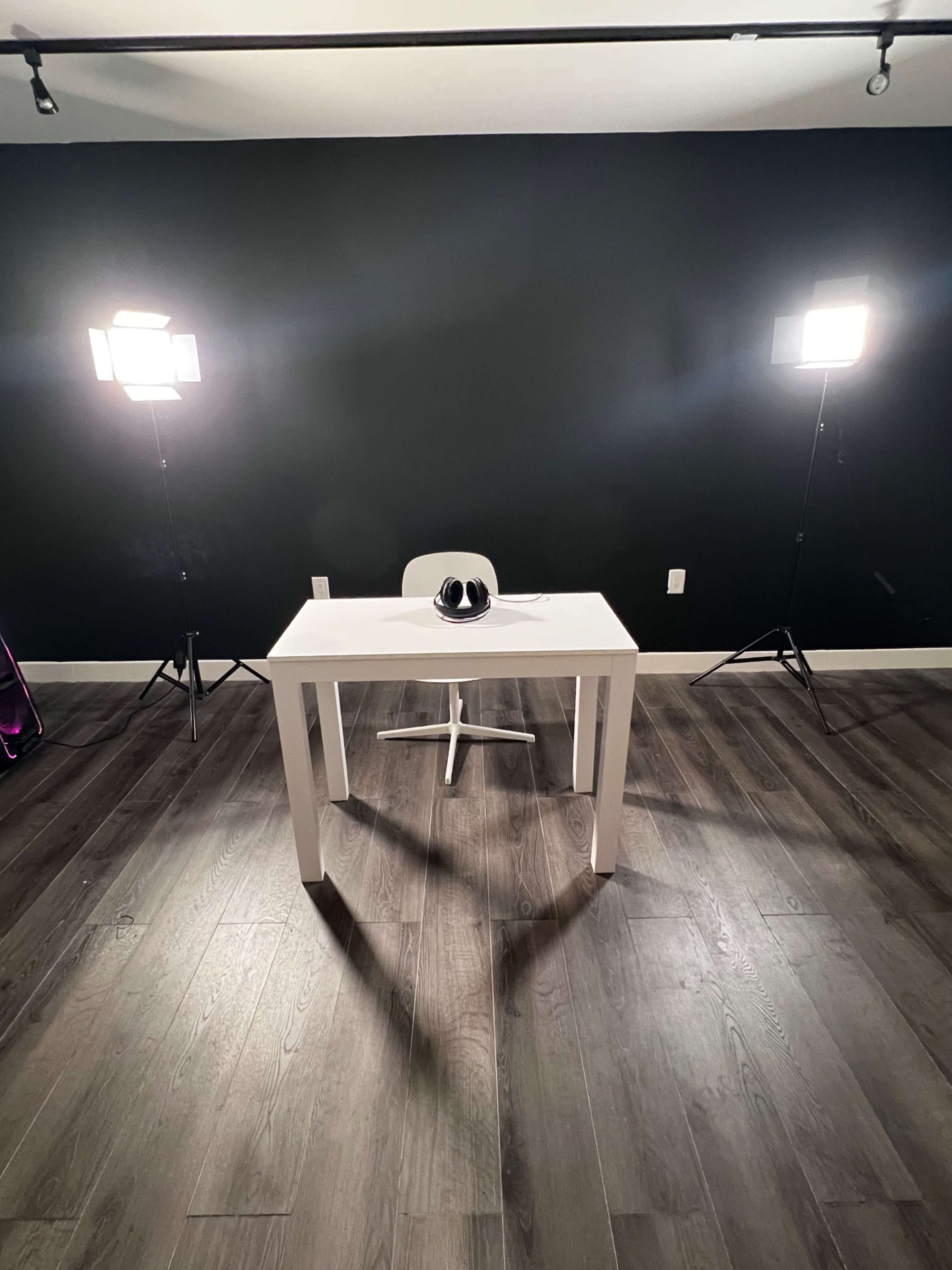 A white table and a chair are positioned in a well-lit room with a black wall and wooden flooring.
