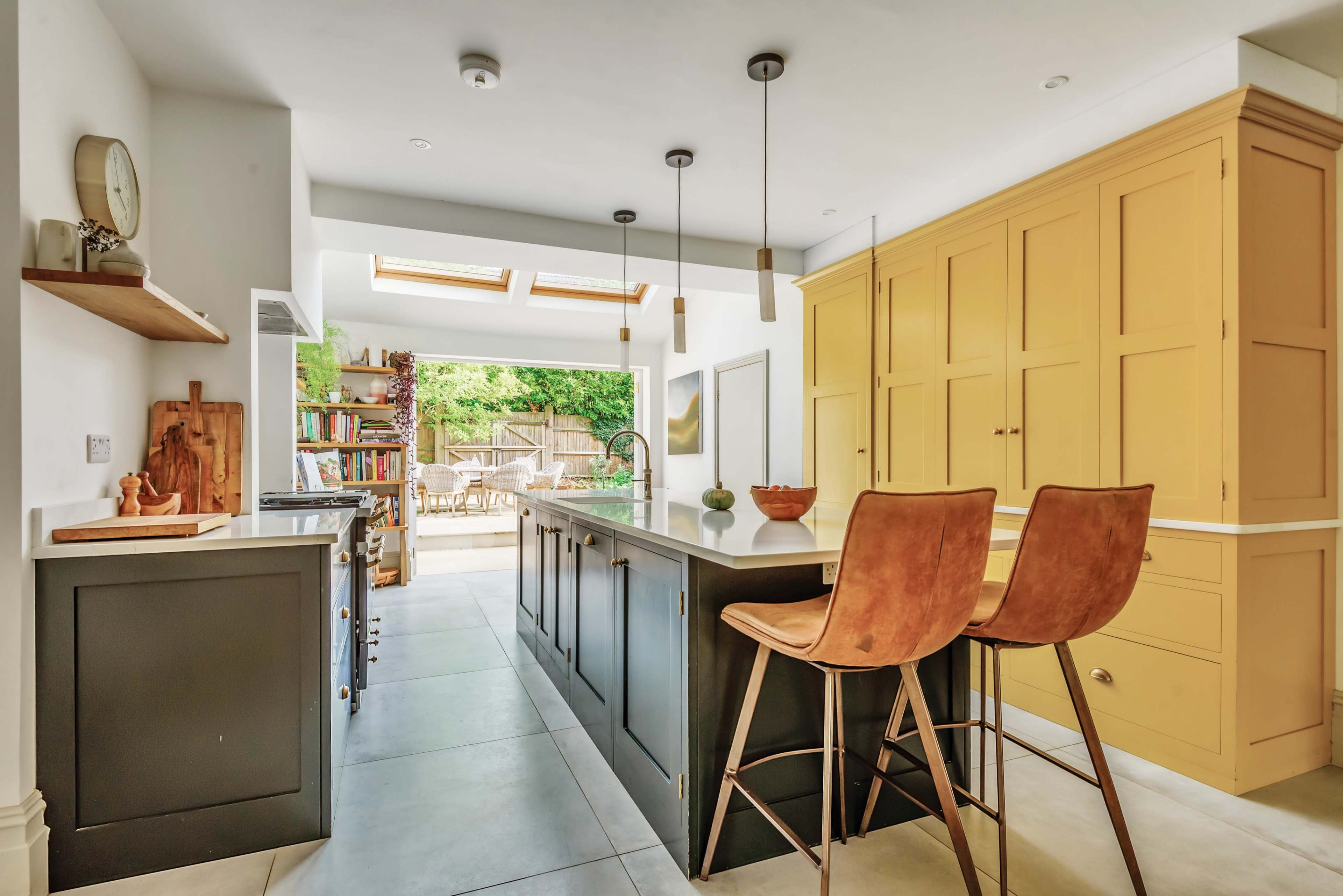 The kitchen features a central island with bar stools, yellow cabinetry, and large skylights providing natural light.