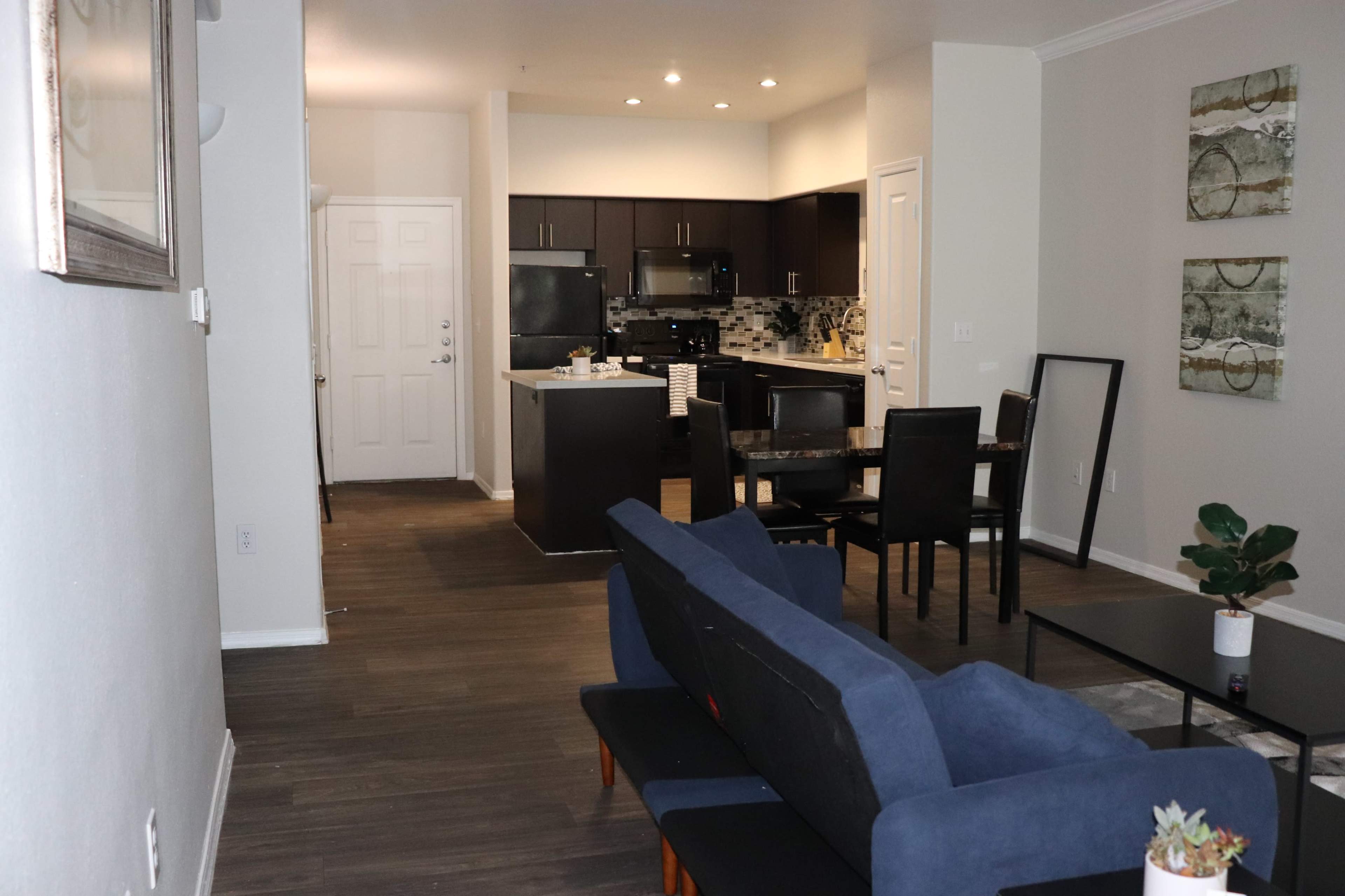 The image shows a modern living space with a blue couch facing a dining area and an open kitchen in the background.