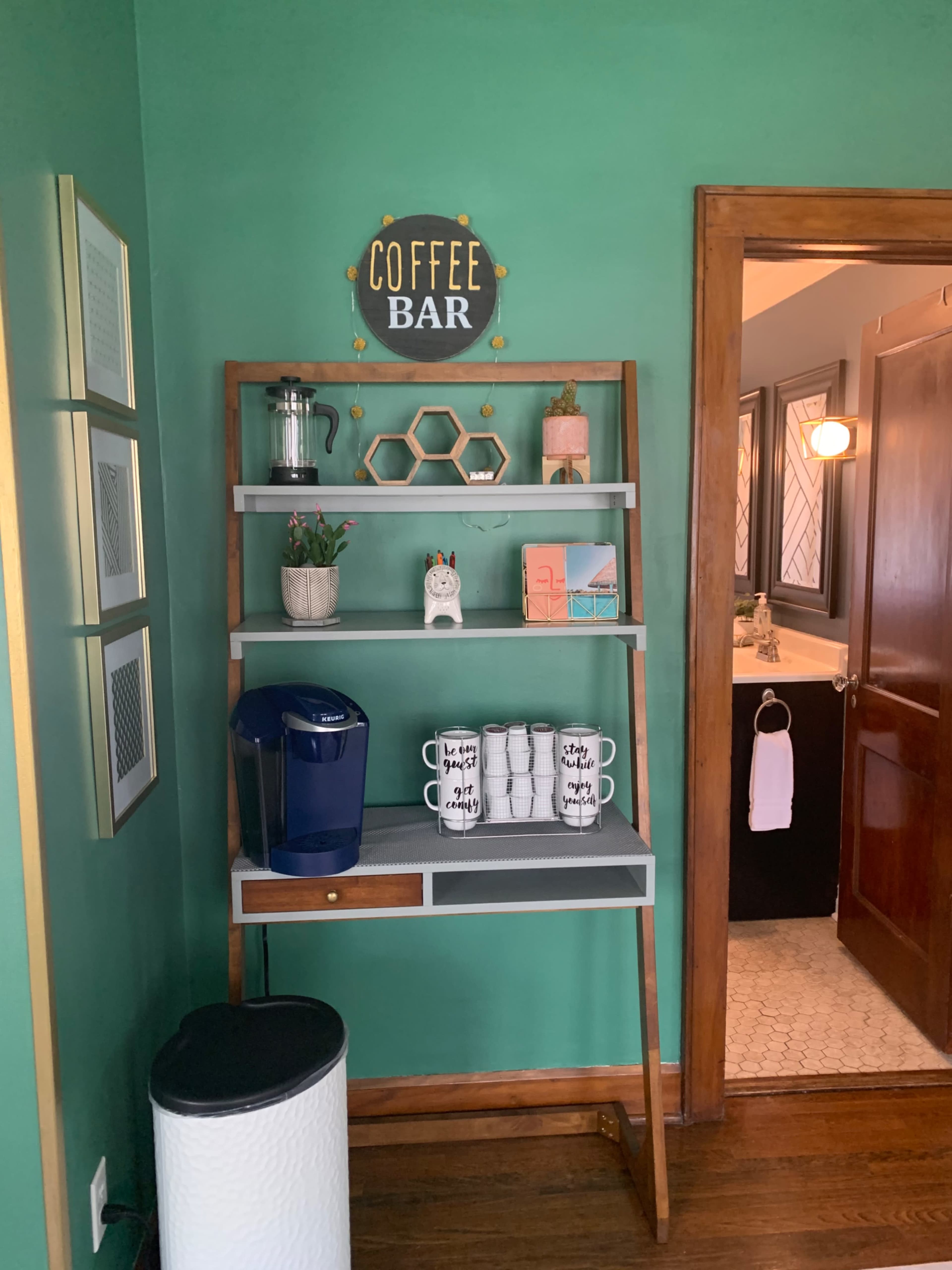 A wooden shelving unit displaying coffee supplies and decorative items against a green wall, with a sign that reads "COFFEE BAR."