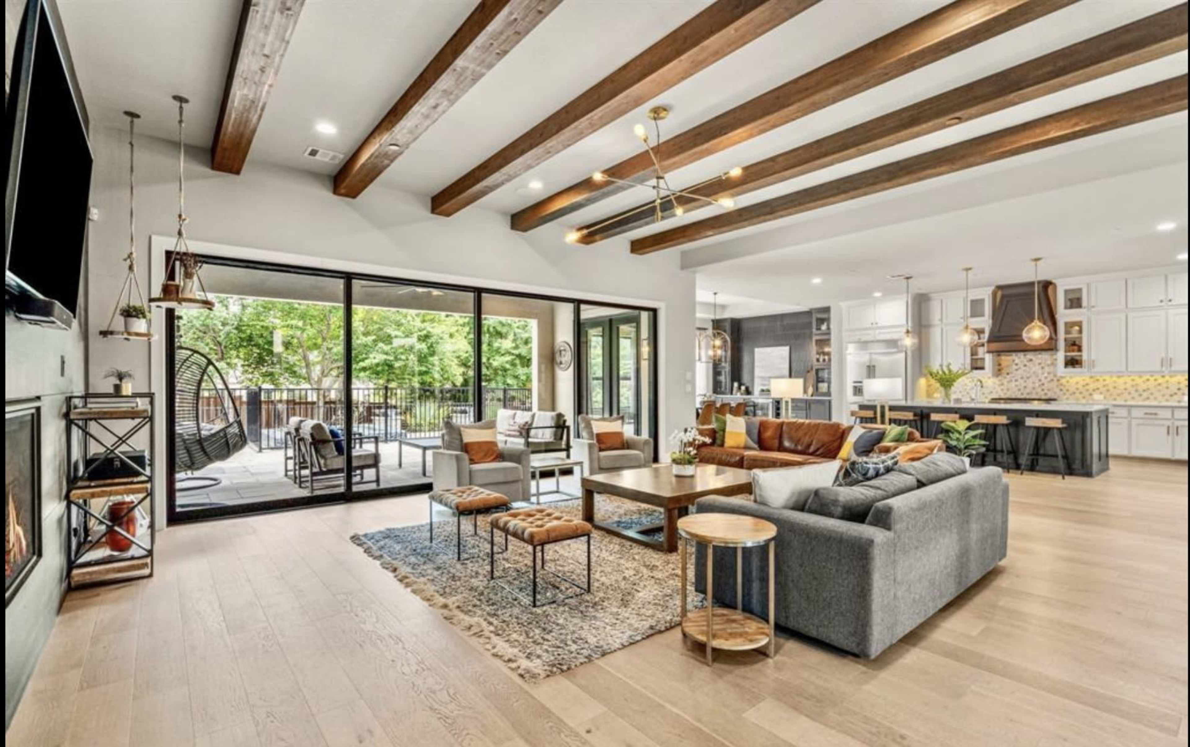 The image features a modern living room with wooden beams, a large sectional sofa, and a view of an outdoor patio through sliding glass doors.