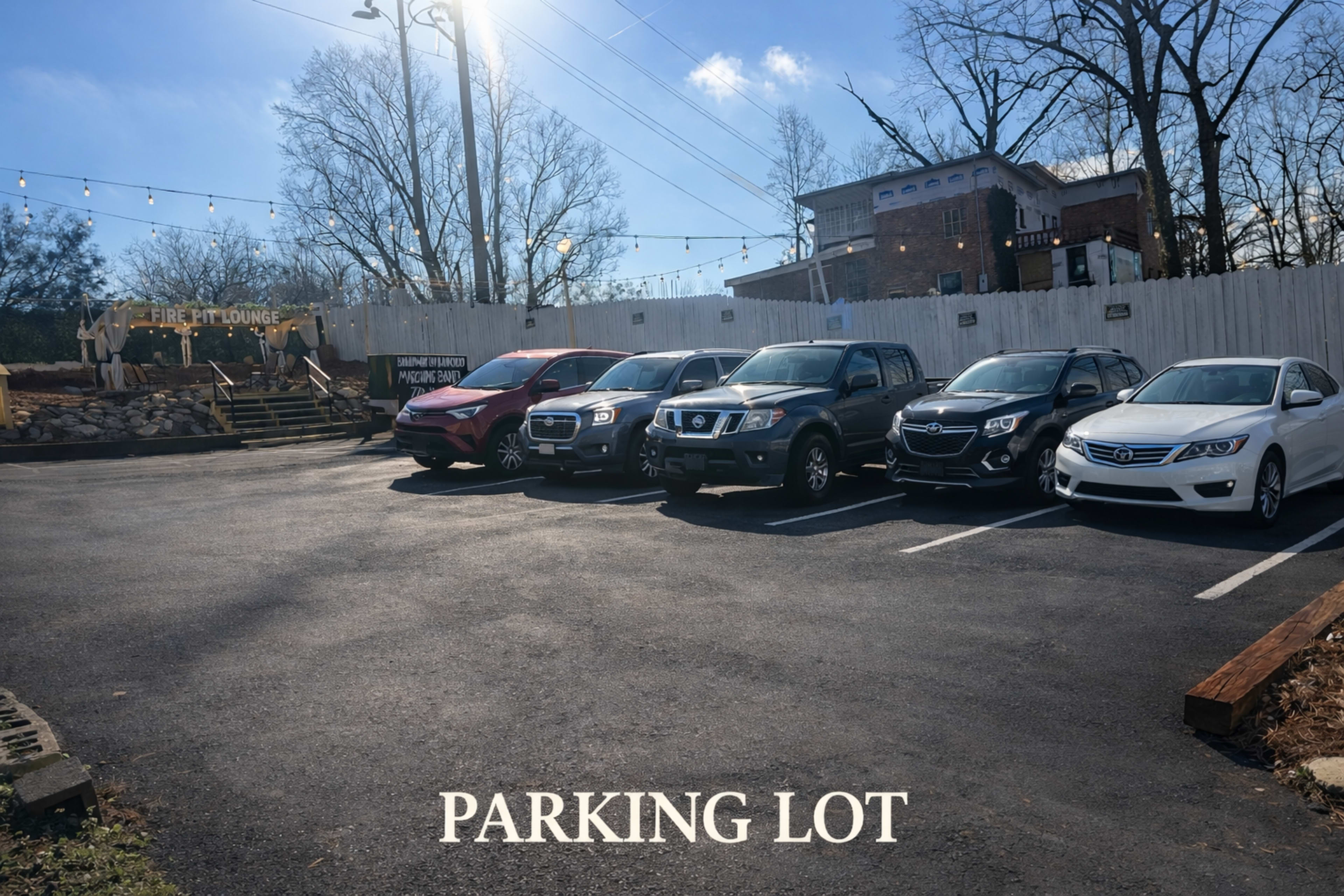 A row of parked vehicles occupies a parking lot adjacent to a building with a sign reading "Fire Pit Lounge."