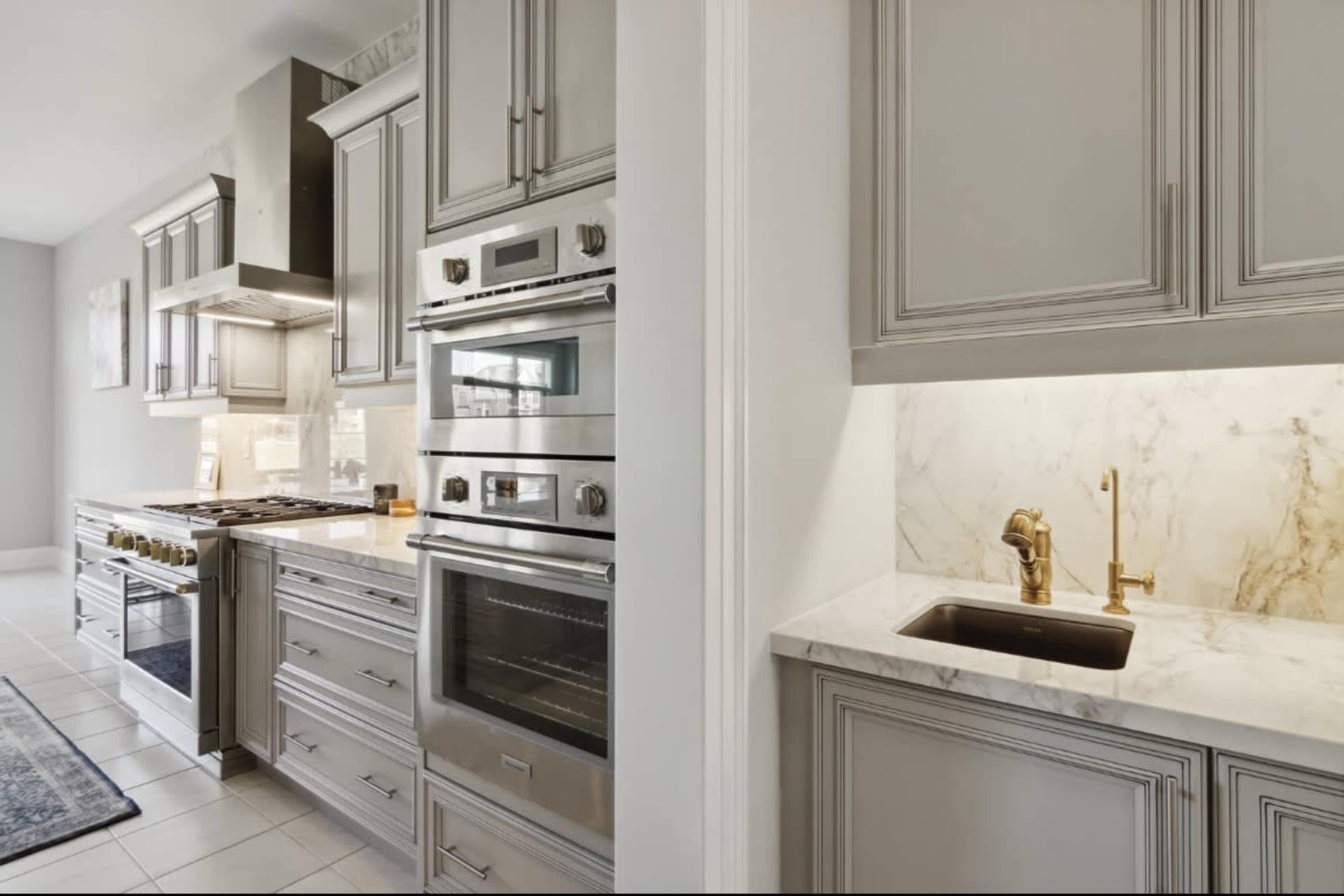 The image shows a modern kitchen featuring stainless steel appliances, including an oven and a stove, with gray cabinetry and marble countertops.