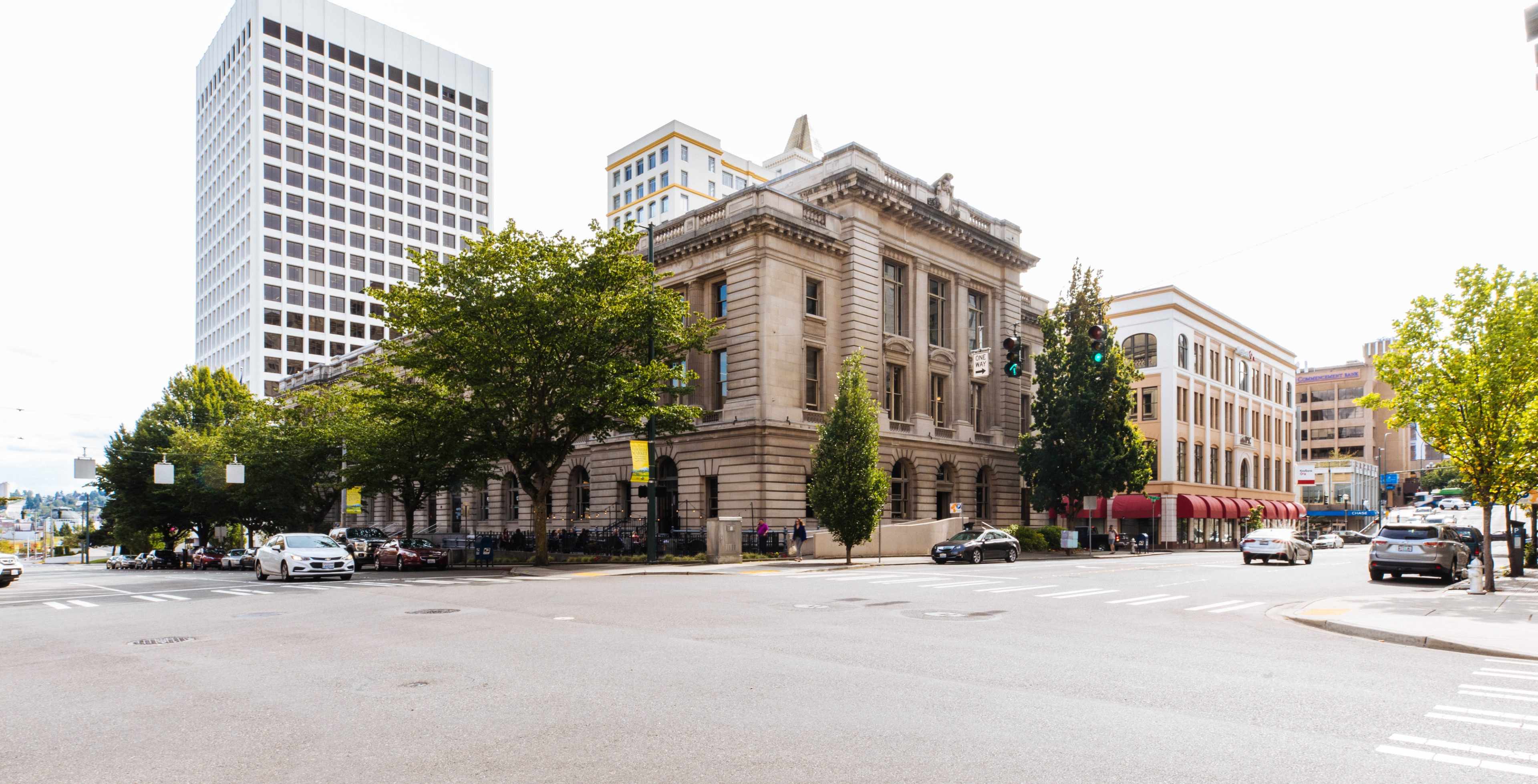 A city intersection featuring a historic building on the corner, flanked by modern high-rises and trees.
