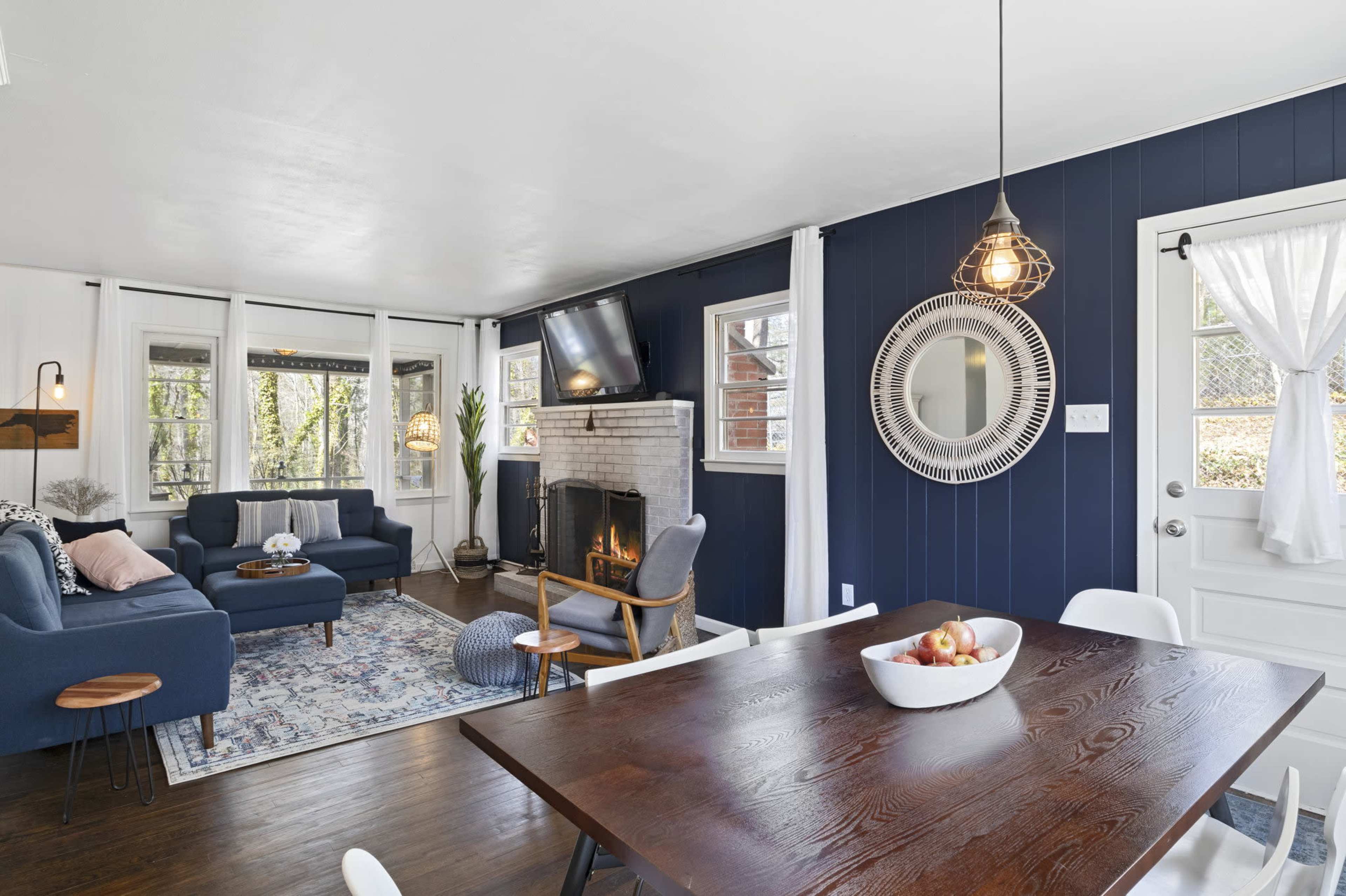 A cozy living area with a fireplace, navy blue walls, a wooden dining table, and large windows allowing natural light.