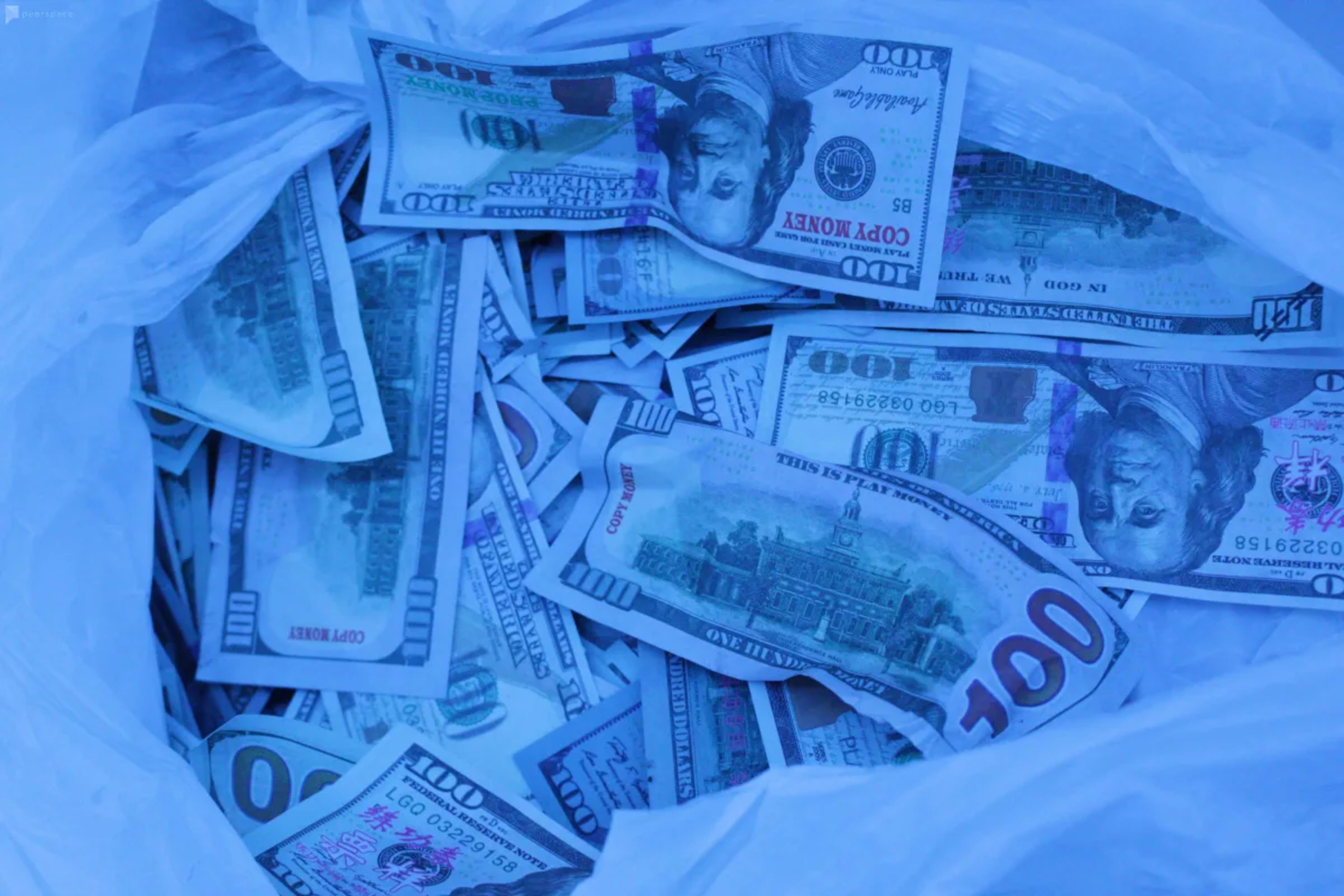 A bag contains numerous packaged $100 bills.