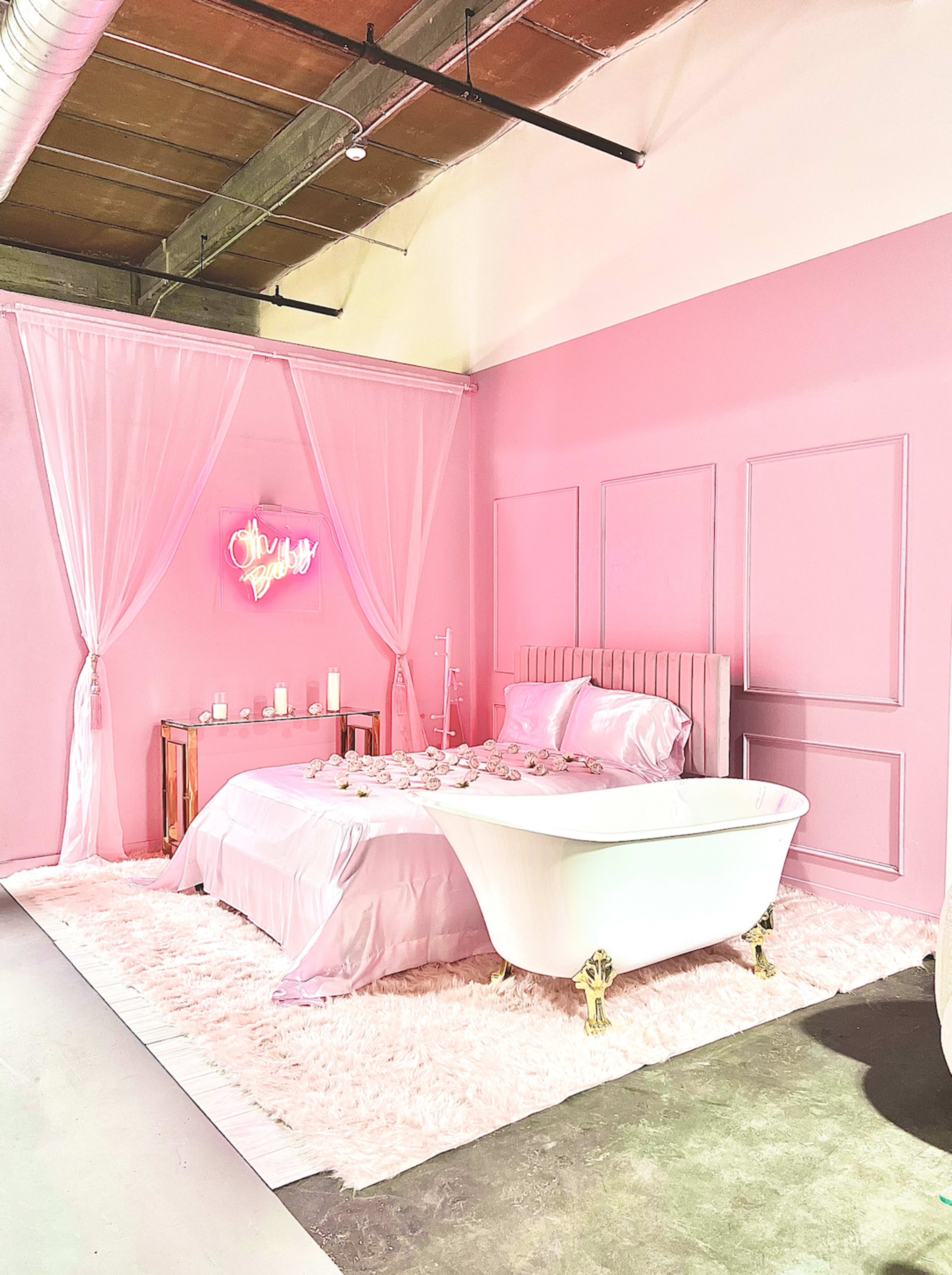 The scene features a pink-themed bedroom with a clawfoot bathtub, a bed adorned with silky linens, and decorative elements like candles on a side table.