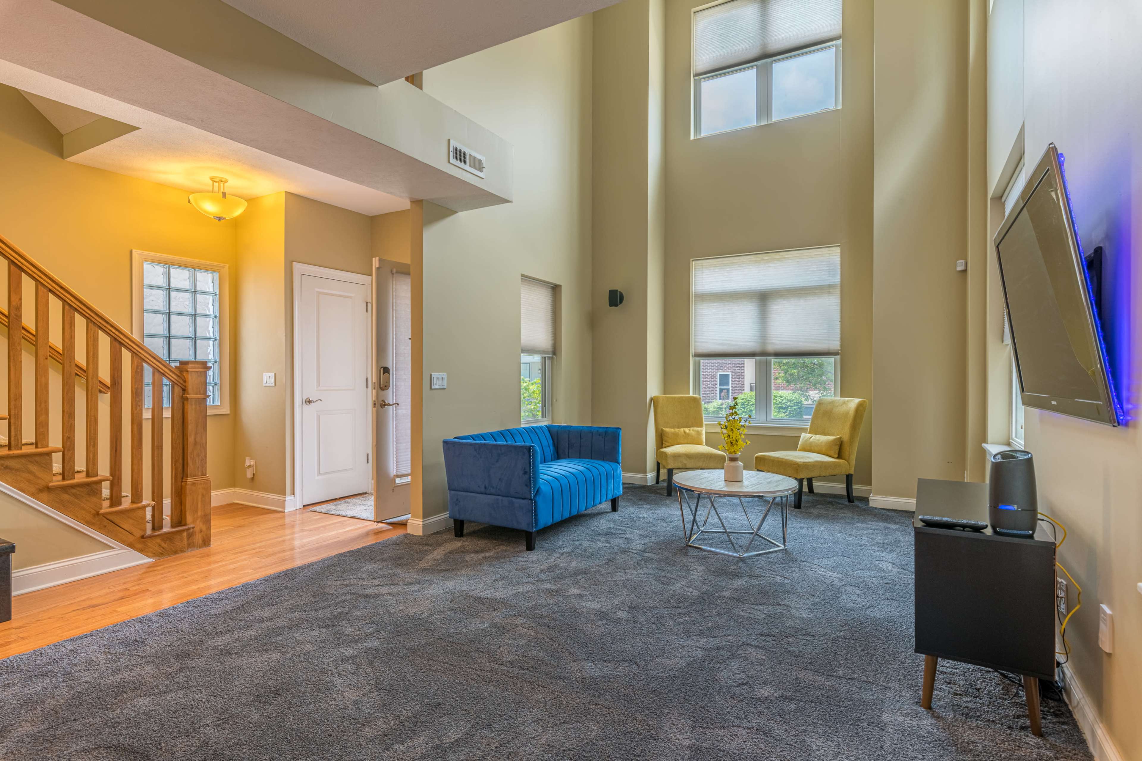The living room features a blue sofa, a round coffee table, and tall windows that allow natural light to fill the space.