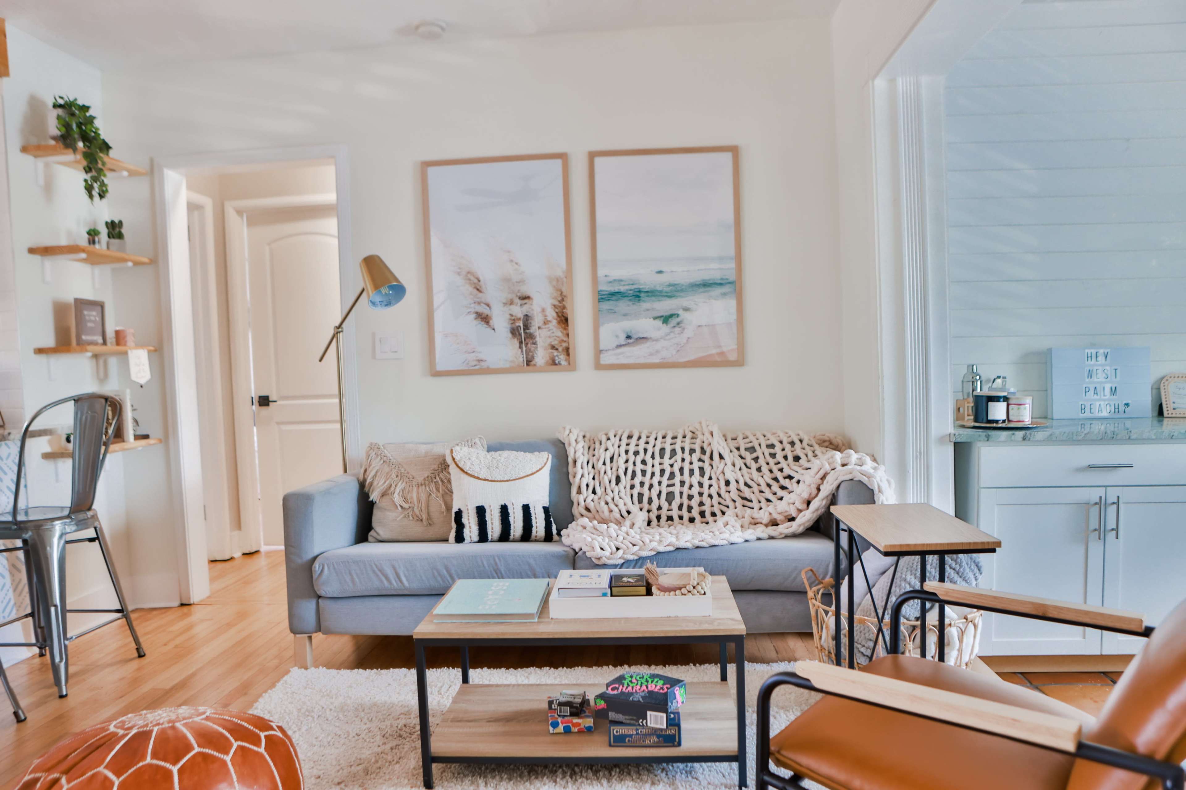 A cozy living room with a gray sofa, a wooden coffee table, and light-colored walls adorned with two framed beach-themed pictures.