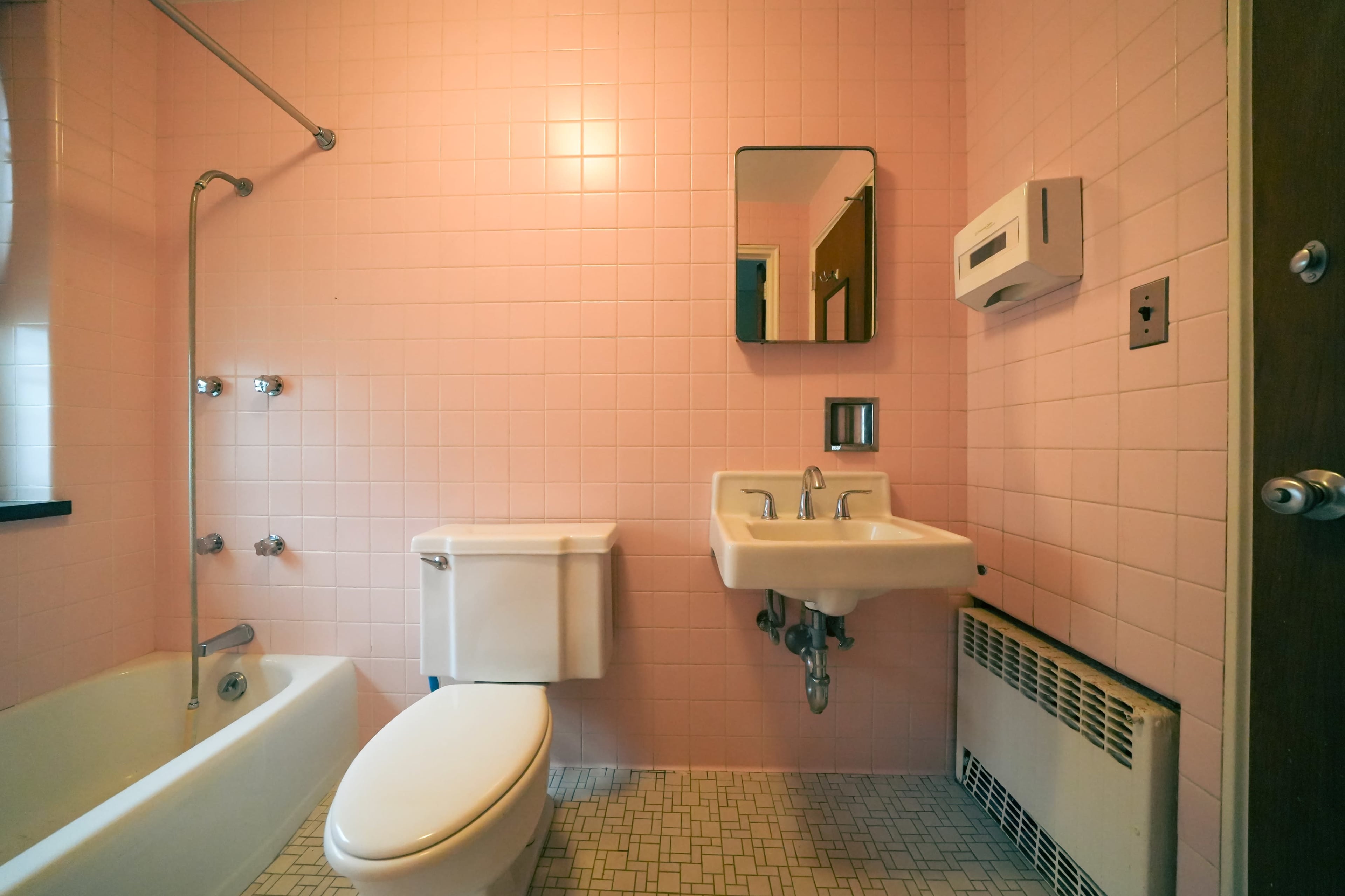 A pink-tiled bathroom with a bathtub, toilet, small sink, and a mirror on the wall.