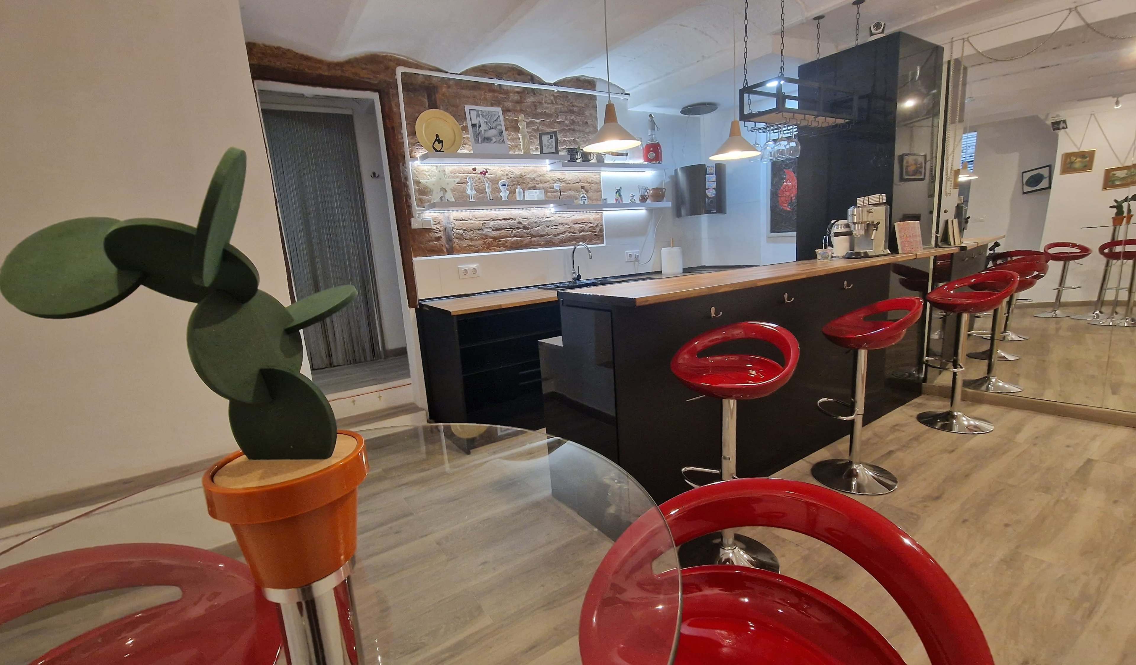 A modern kitchen and dining area featuring a bar counter with high red stools, a potted plant sculpture, and a brick accent wall.