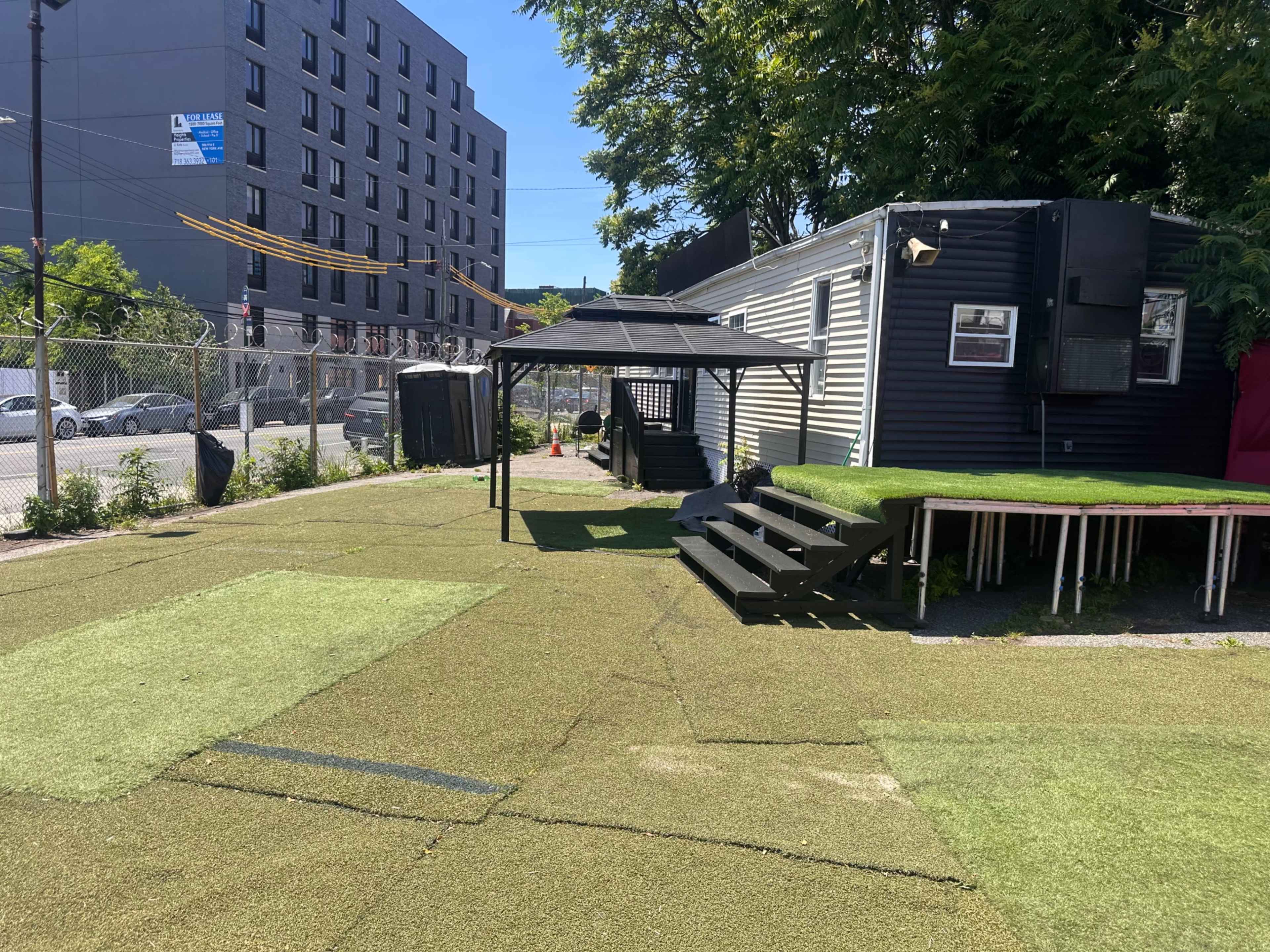 The image shows a grassy area with artificial turf, a gazebo, and steps leading to a building with a dark exterior.
