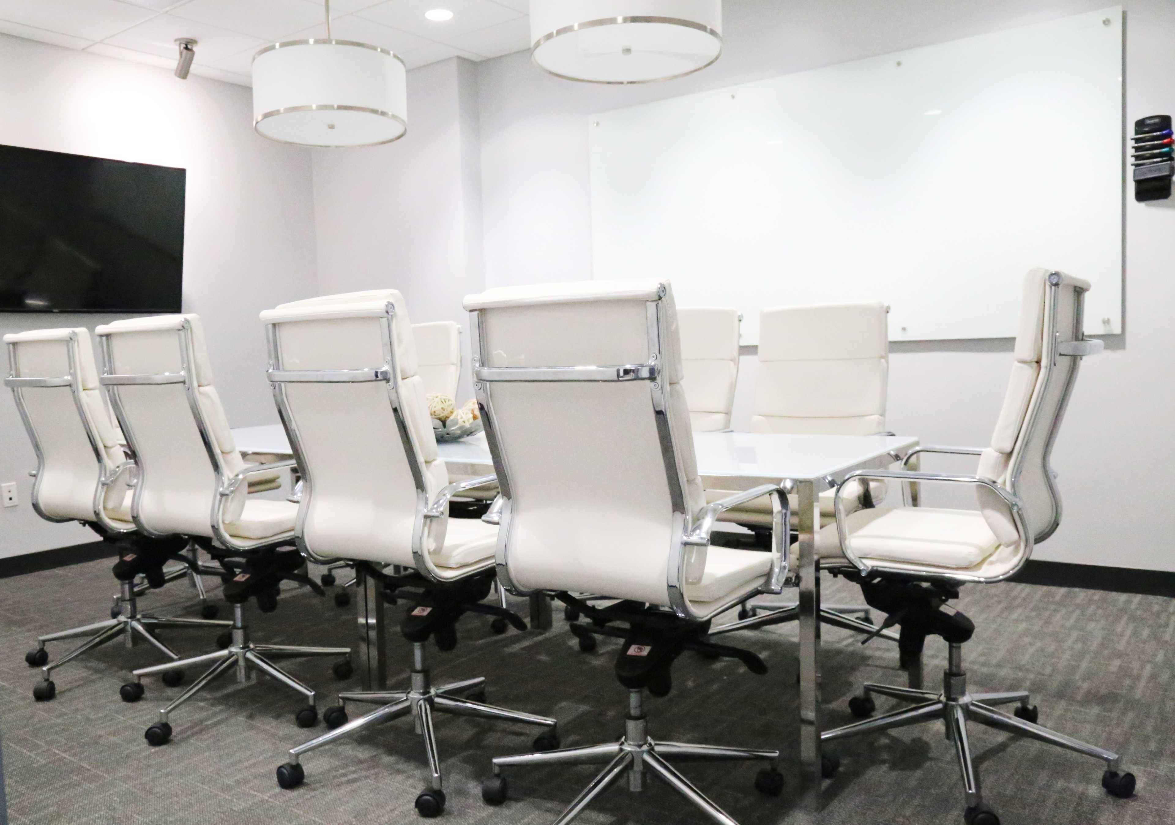 A modern conference room features a large table surrounded by white ergonomic chairs and minimalistic decor.