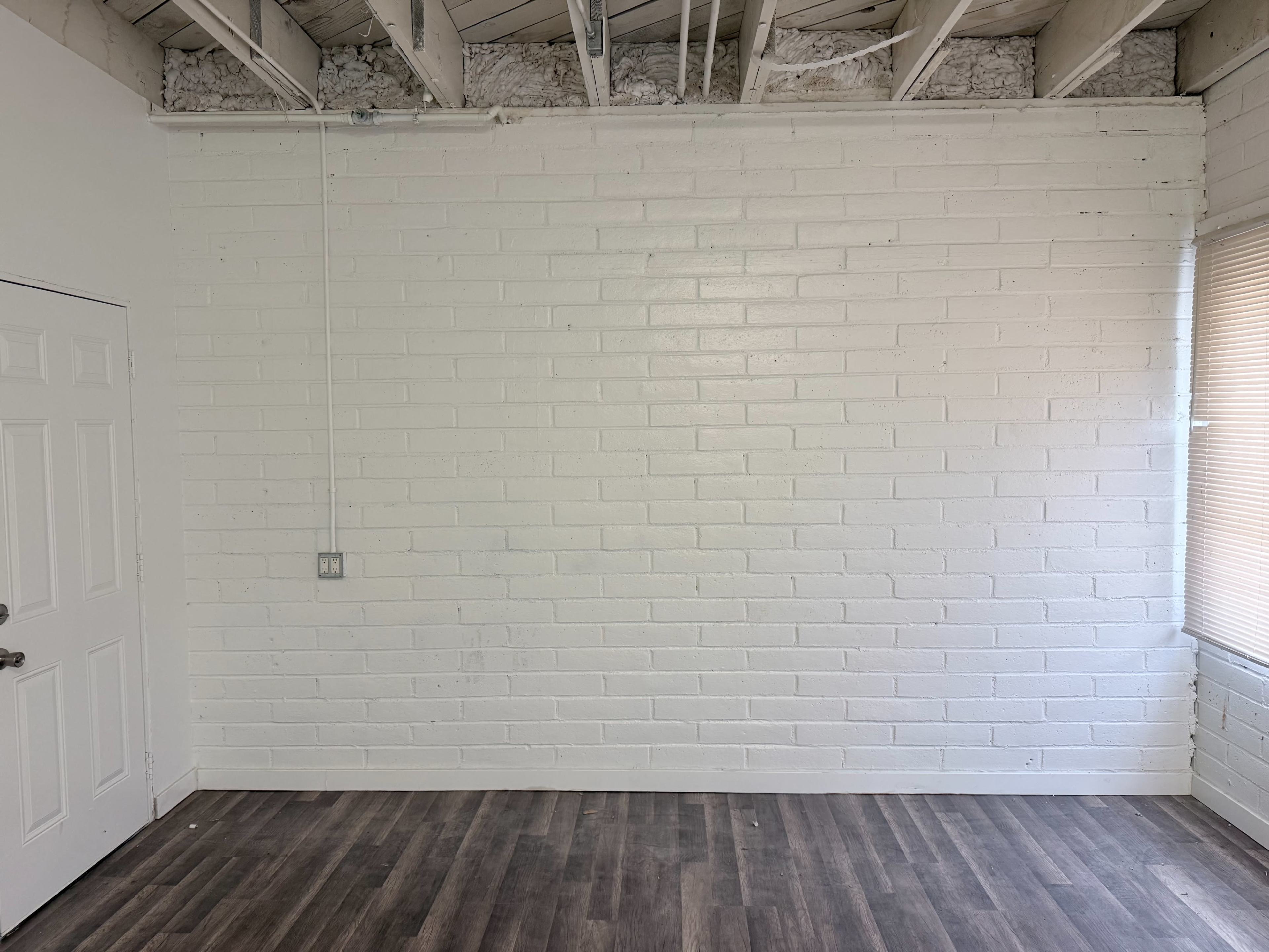 The image shows a room with a white brick wall, a door on the left, and a window on the right with wooden flooring.