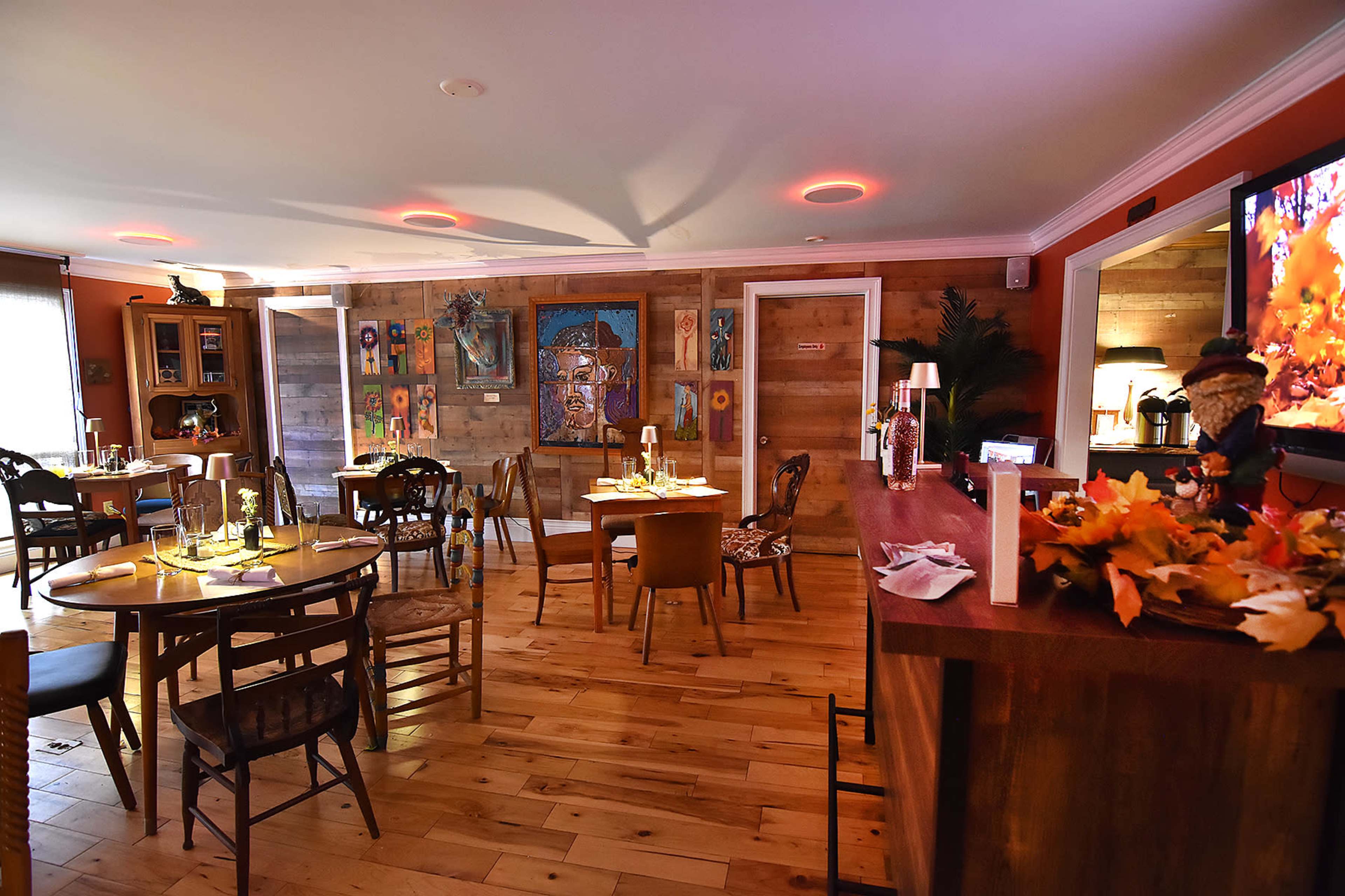 A cozy dining area with wooden floors, several tables set for meals, and colorful artwork on the walls.
