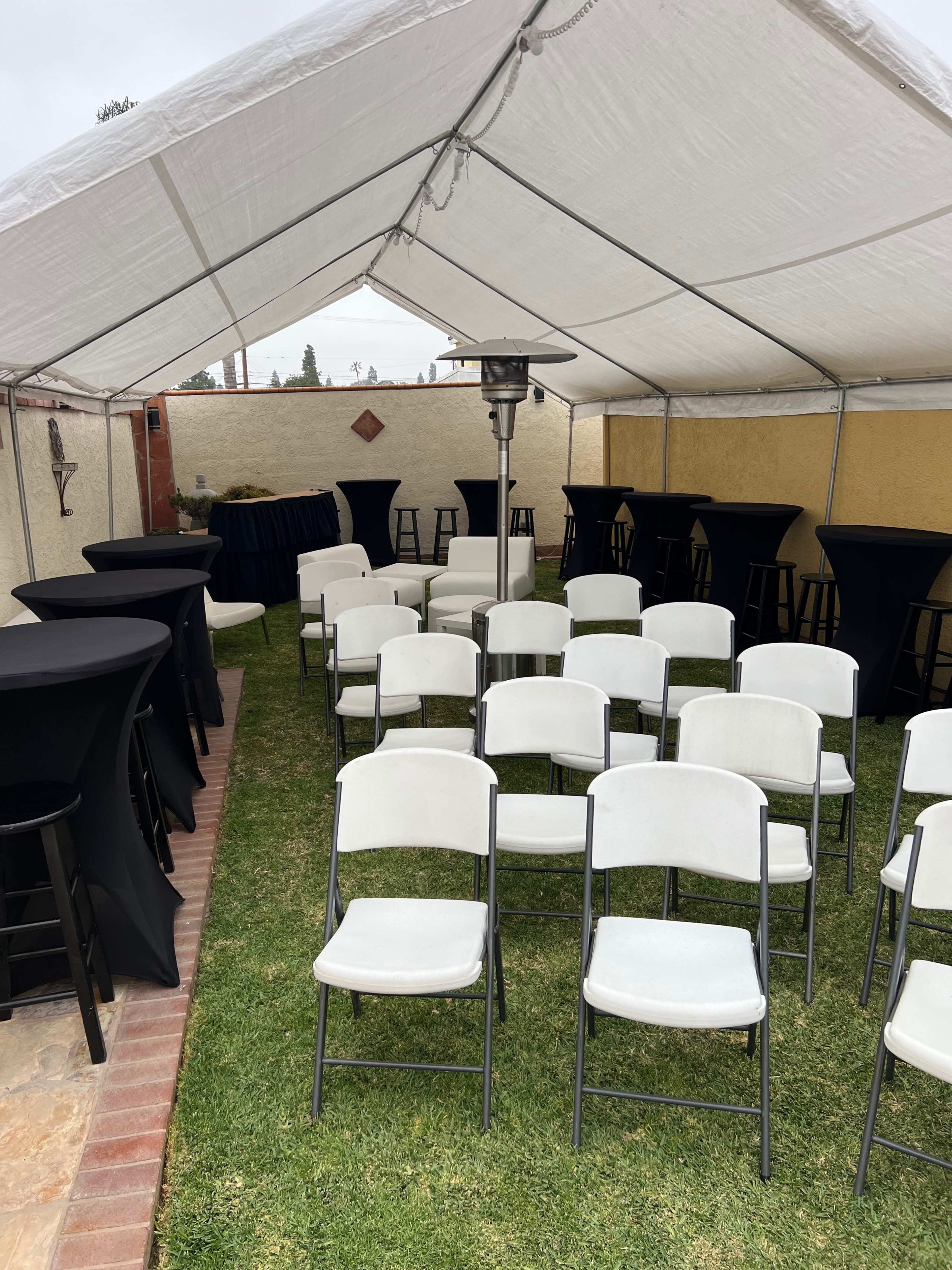 A tent set up with several rows of white folding chairs and black high-top tables on a grassy area.