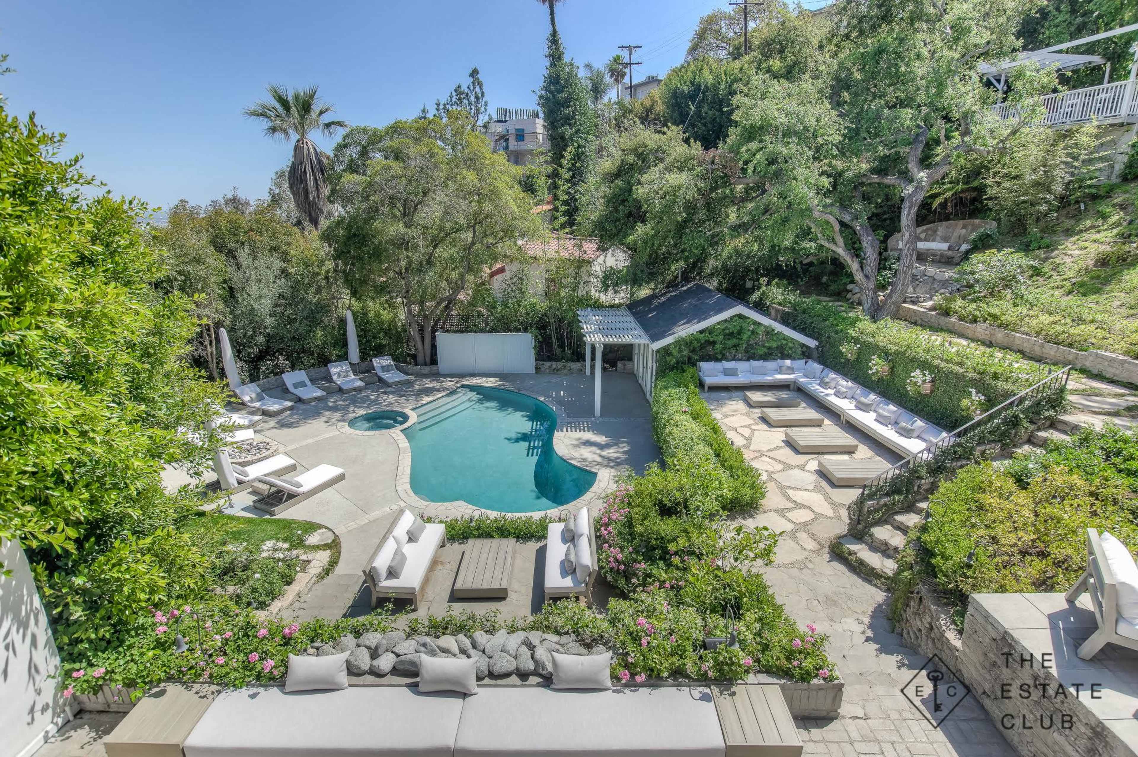 A landscaped backyard featuring a swimming pool, lounge chairs, and seating areas surrounded by greenery.