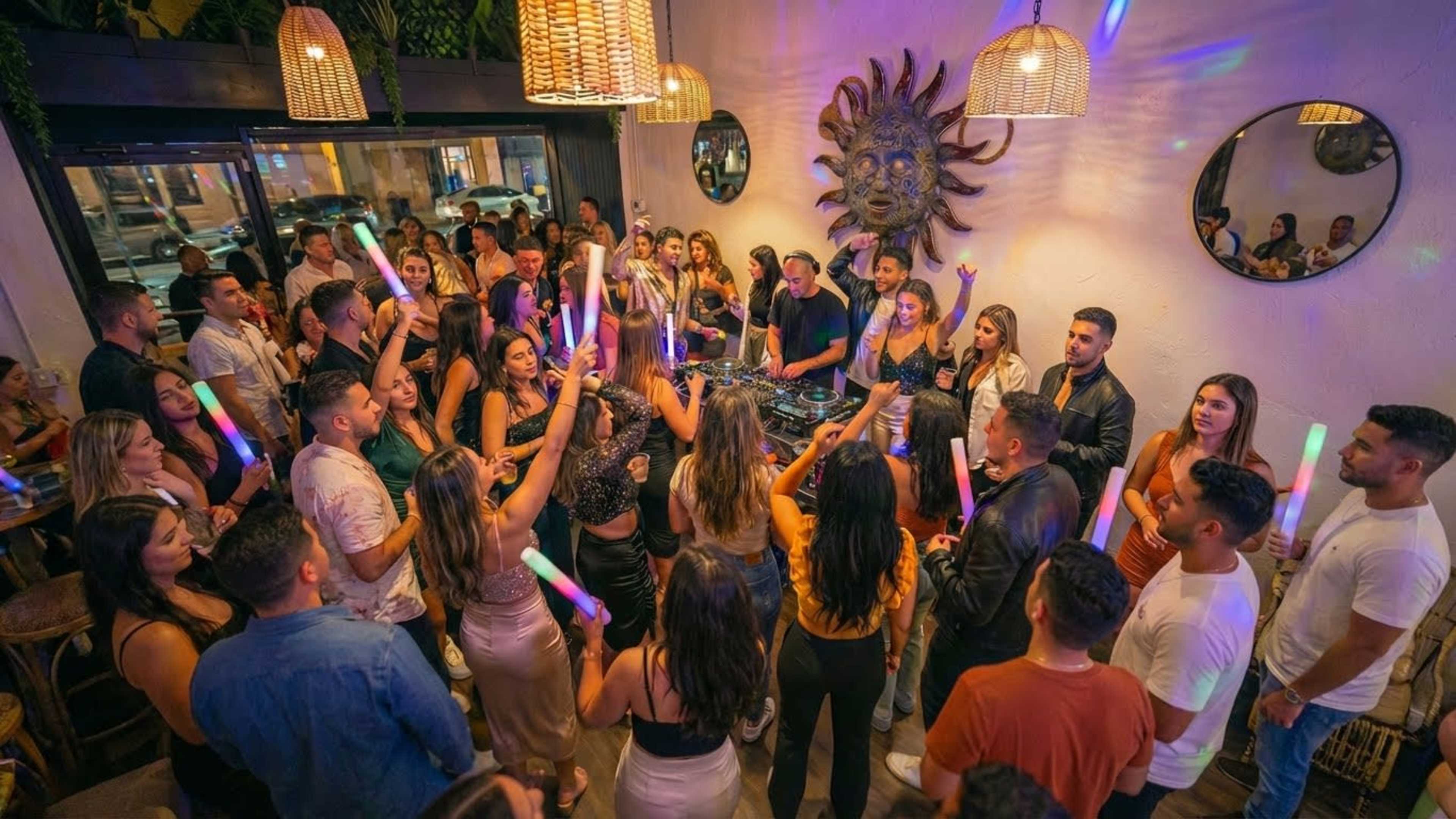 A large group of people is dancing and enjoying music in a lively venue decorated with colorful lights and unique wall art.