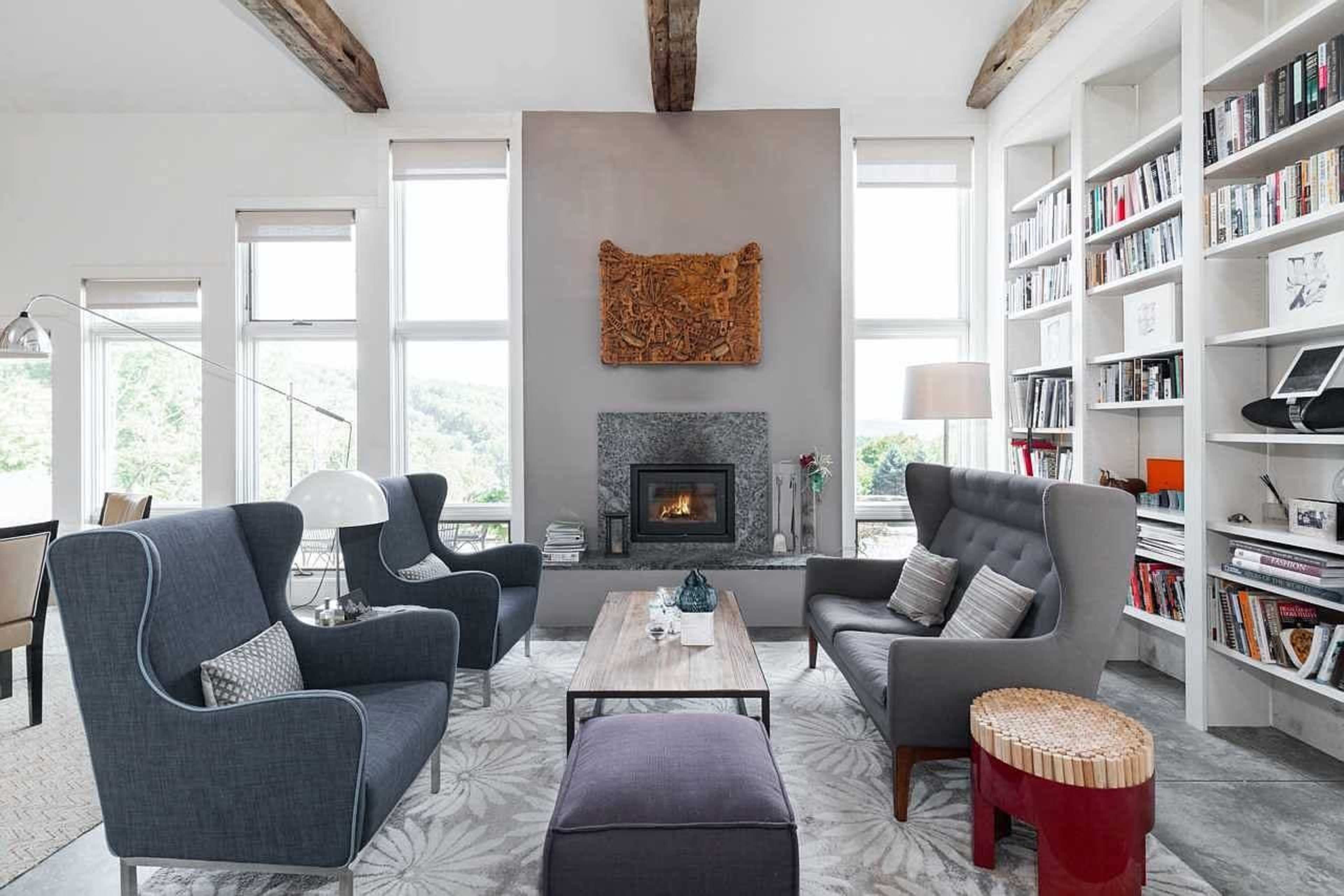 The living room features two armchairs, a sofa, a coffee table, a fireplace, and a bookshelf, all arranged with large windows providing natural light.