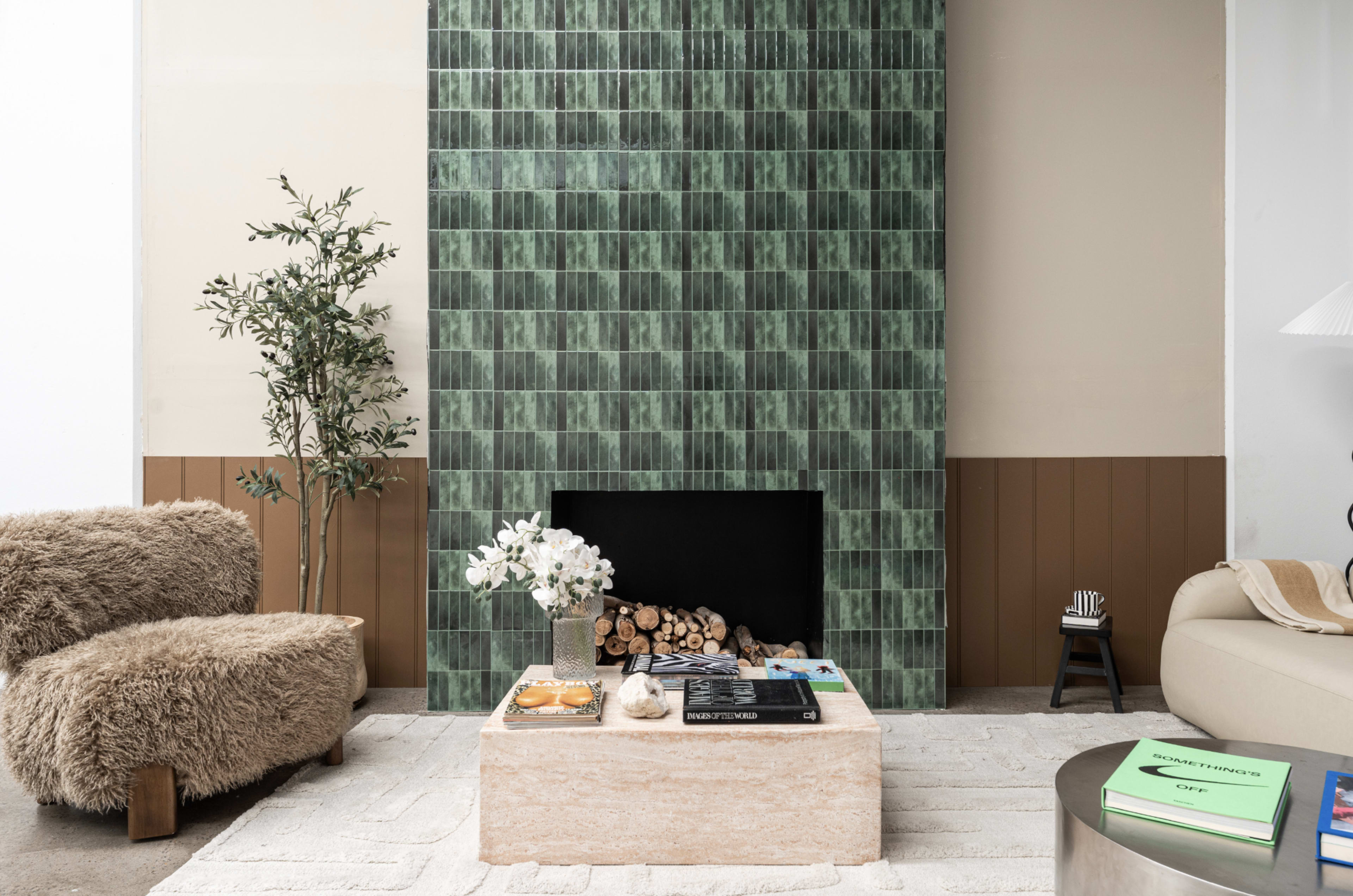 A modern living room features a green tiled fireplace, a stone coffee table, and cozy seating, all accented by a plant and decorative items.
