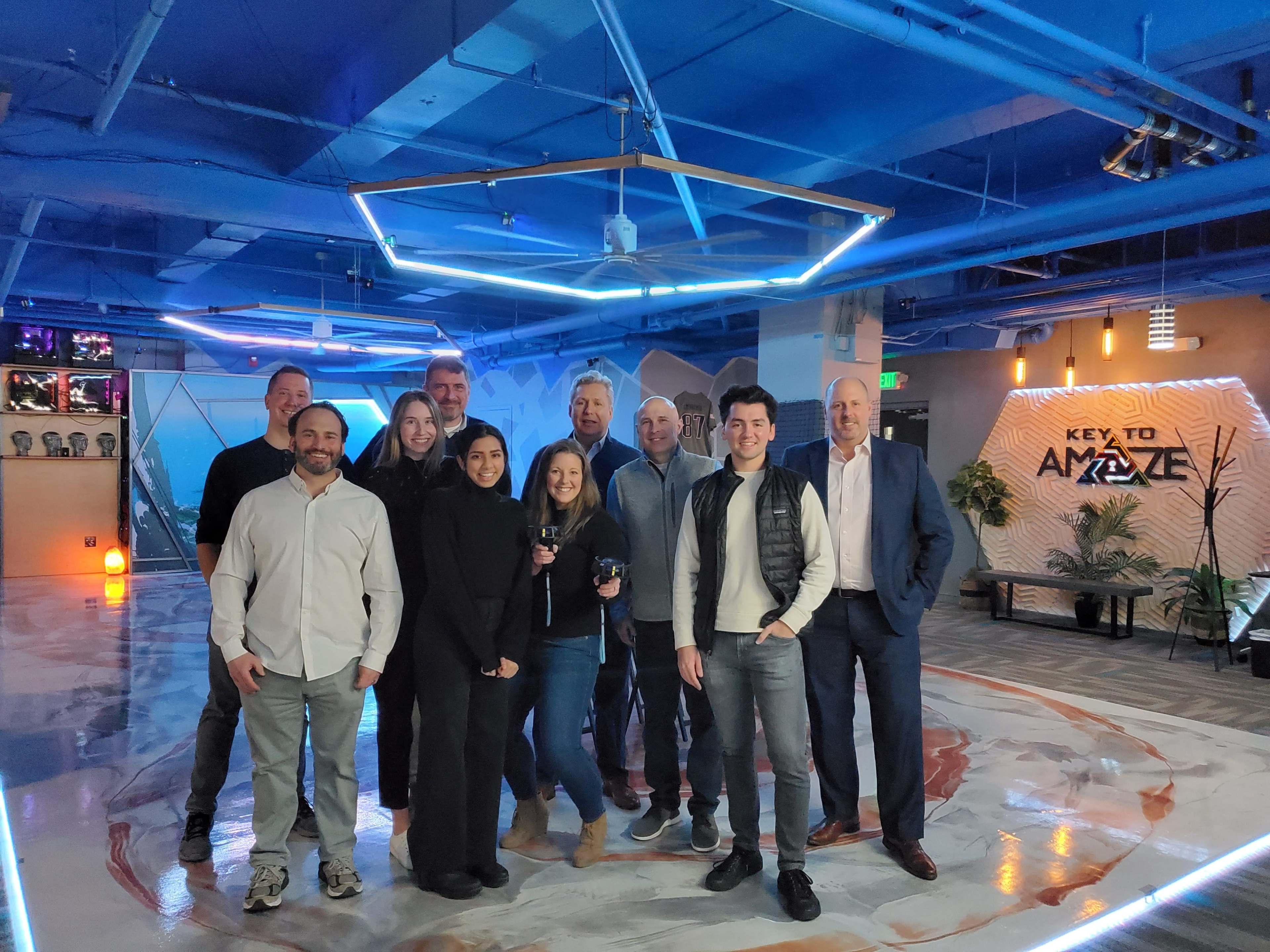 A group of eleven people stands together in a modern office space with bright blue lighting and geometric decor.
