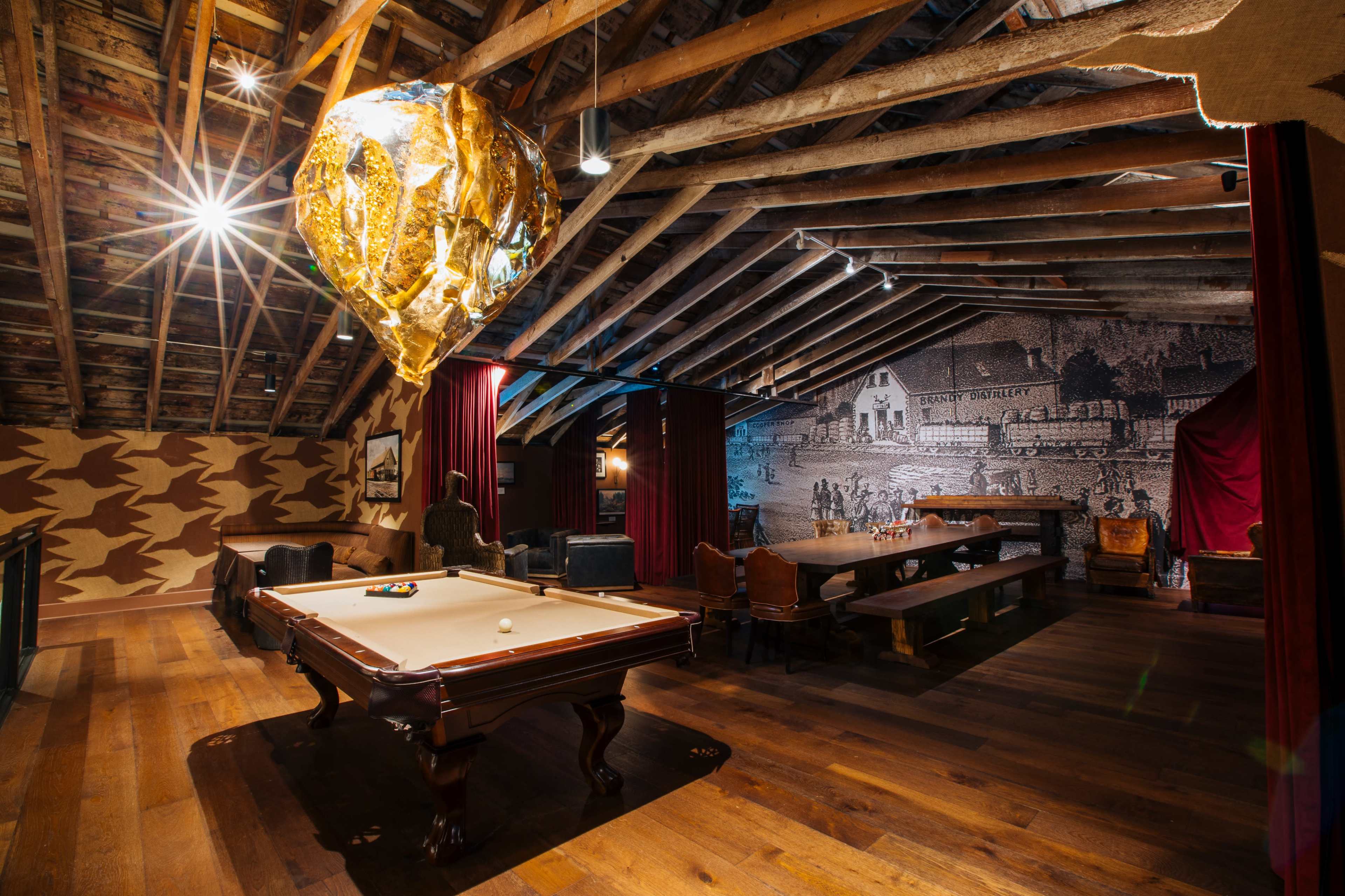 The image shows a rustic game room featuring a pool table, wooden beams overhead, and a large decorative balloon hanging from the ceiling.