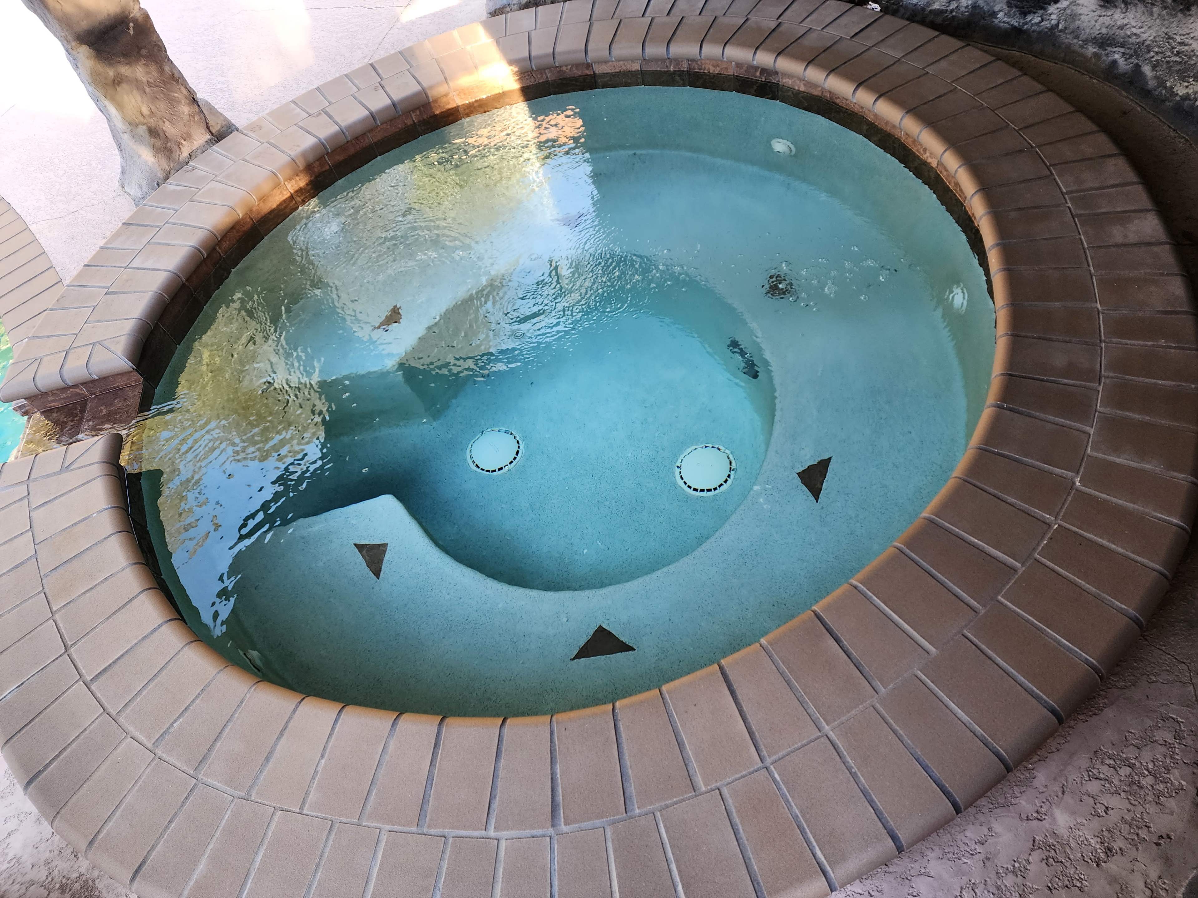 The image shows a circular hot tub with a tiled edge, featuring two circular jets and a smooth, clear water surface.