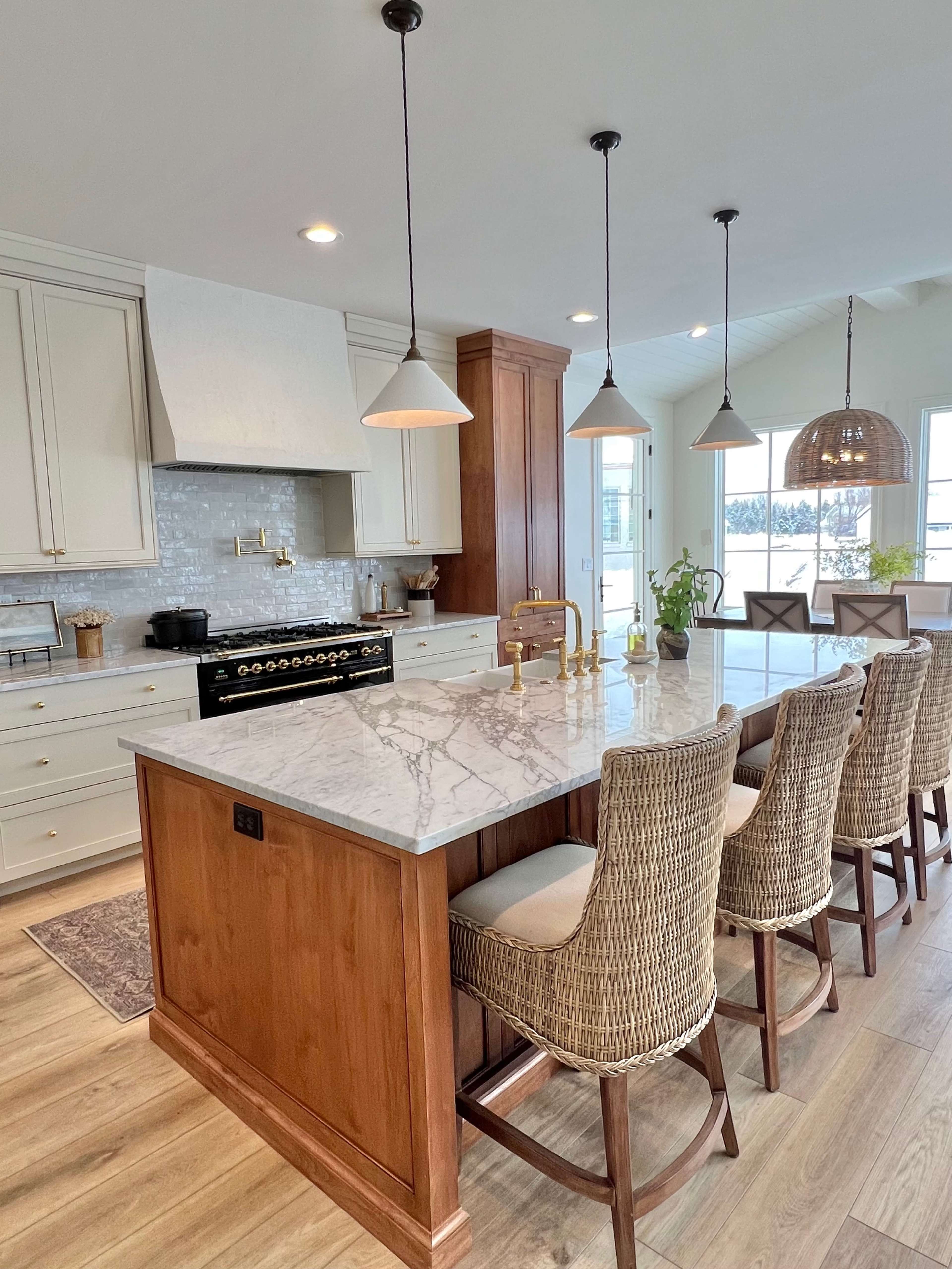 A modern kitchen with a large marble countertop, wooden cabinetry, and a row of woven bar stools.