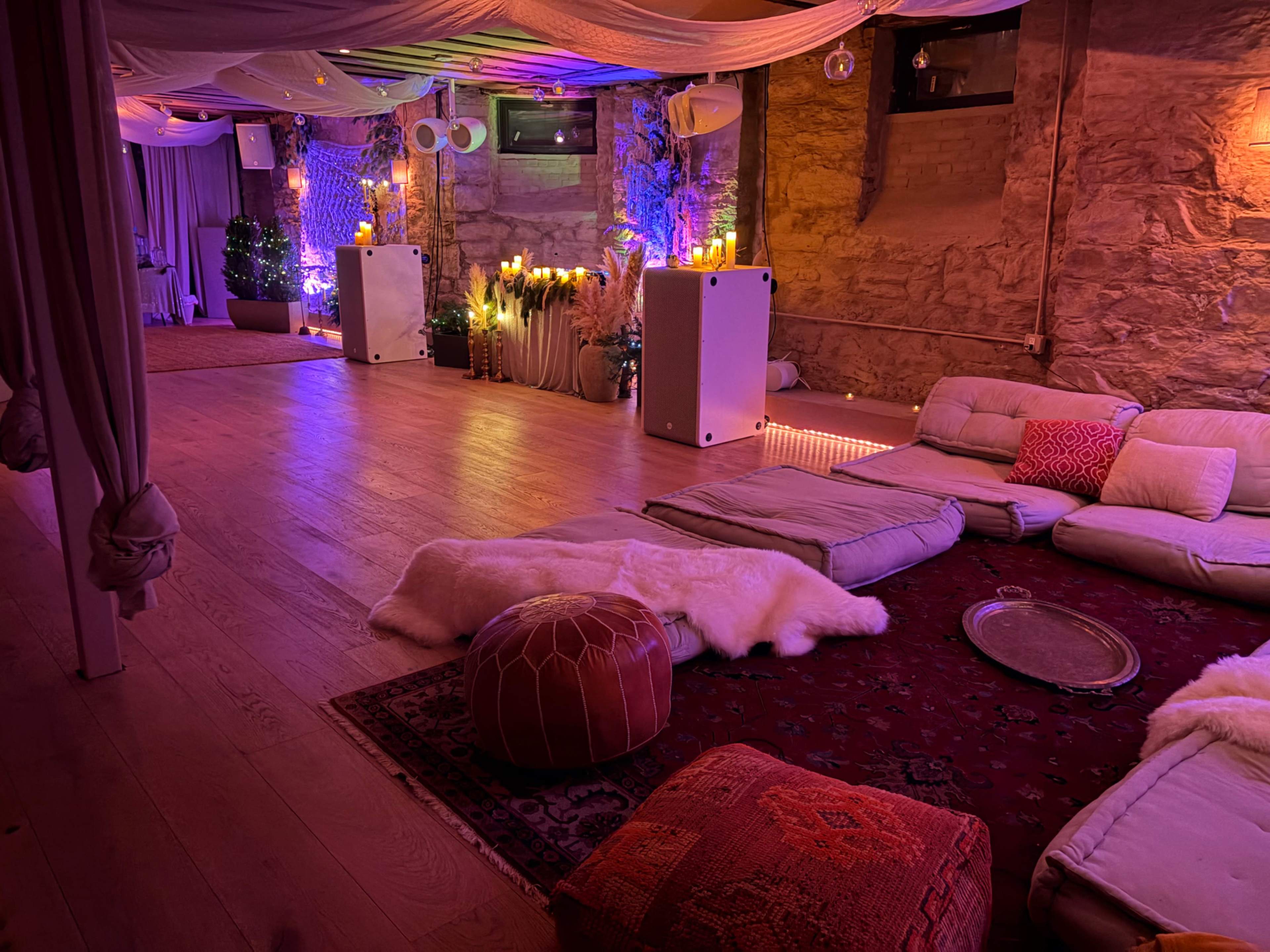 The room features a cozy lounge area with floor cushions, soft rugs, and ambient lighting against stone walls.