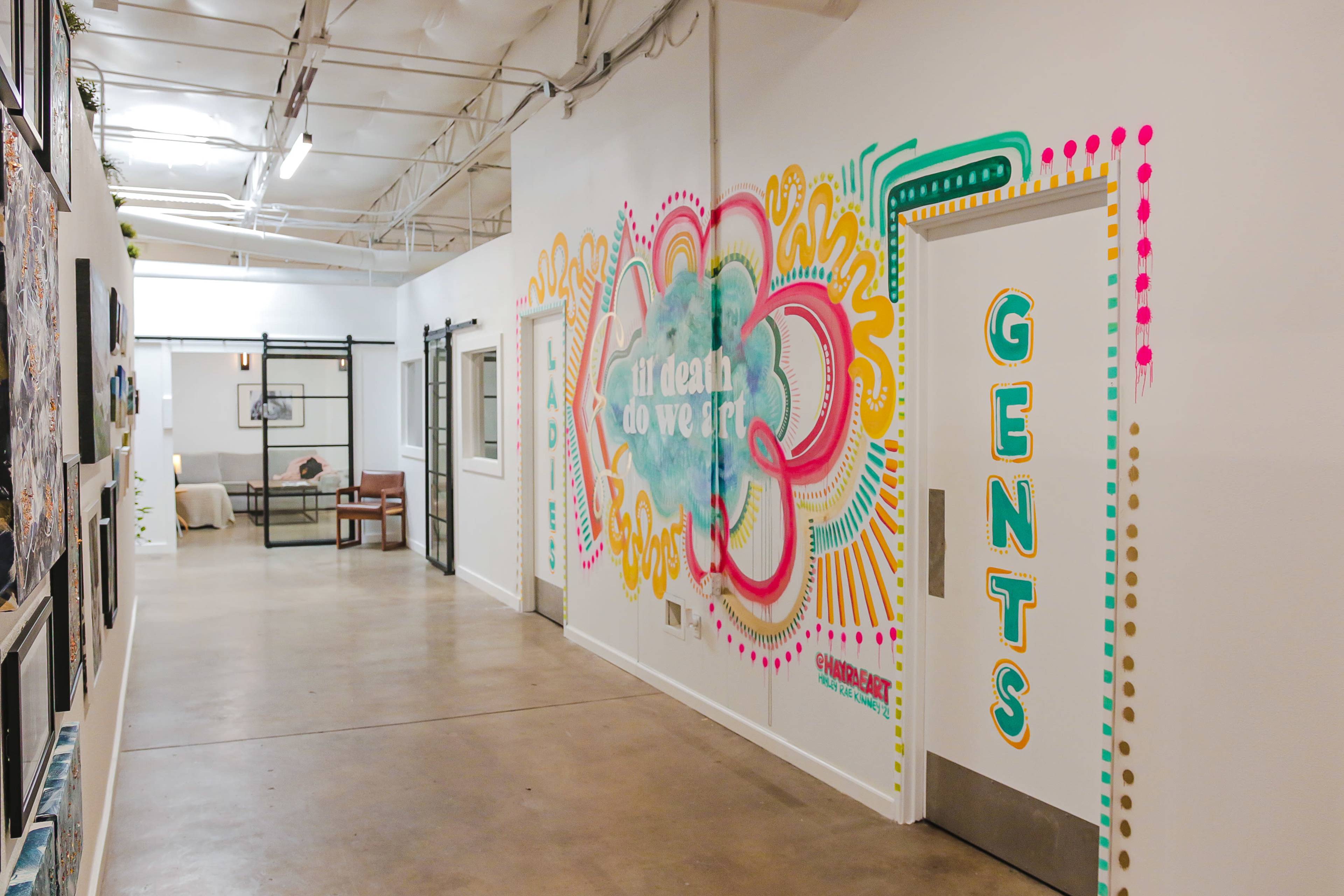 A brightly colored mural and a "GENTS" restroom door are visible along a hallway with artwork displayed on the walls.