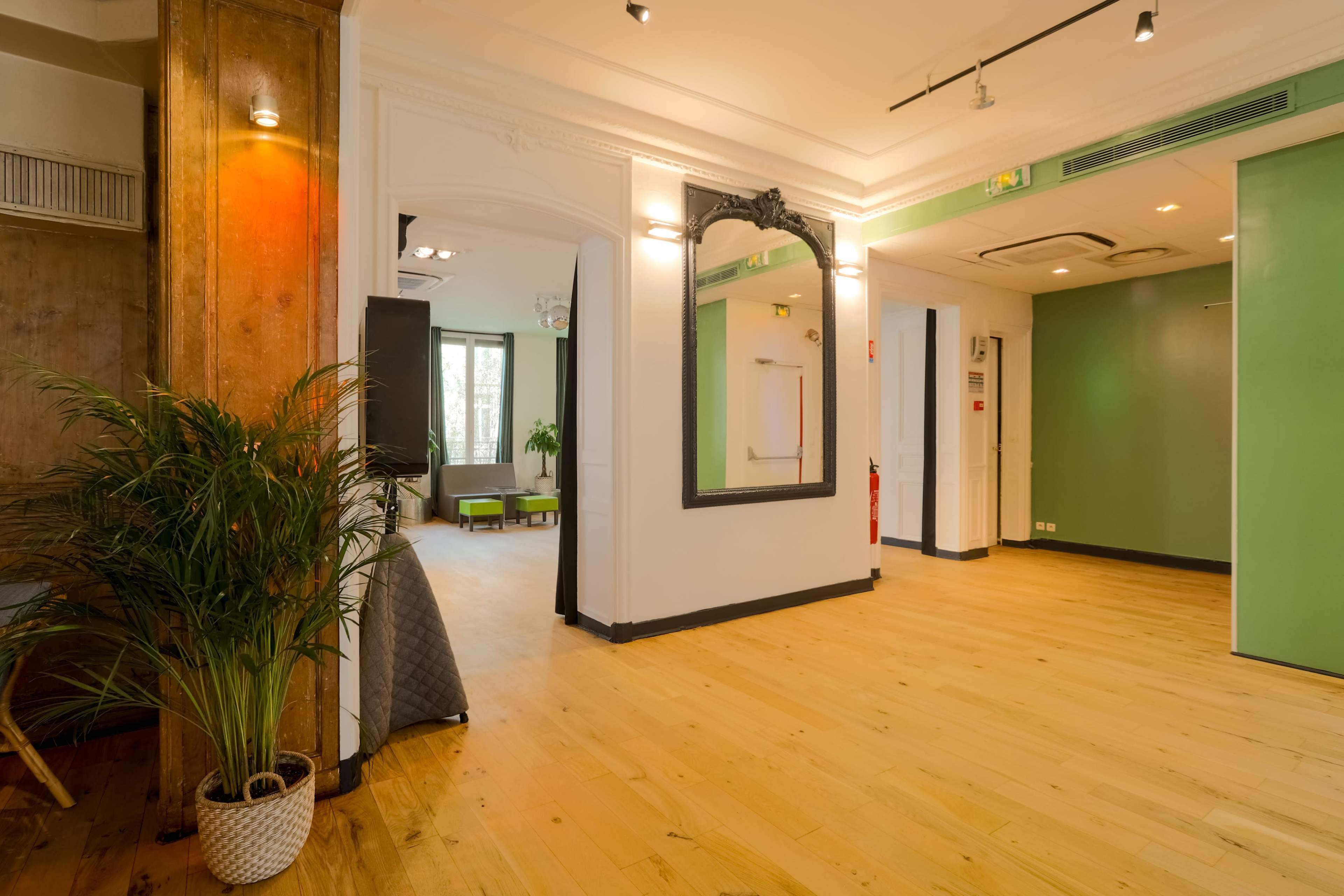 A spacious, well-lit foyer featuring wooden flooring, a large mirror on the wall, and a green accent wall in the background.