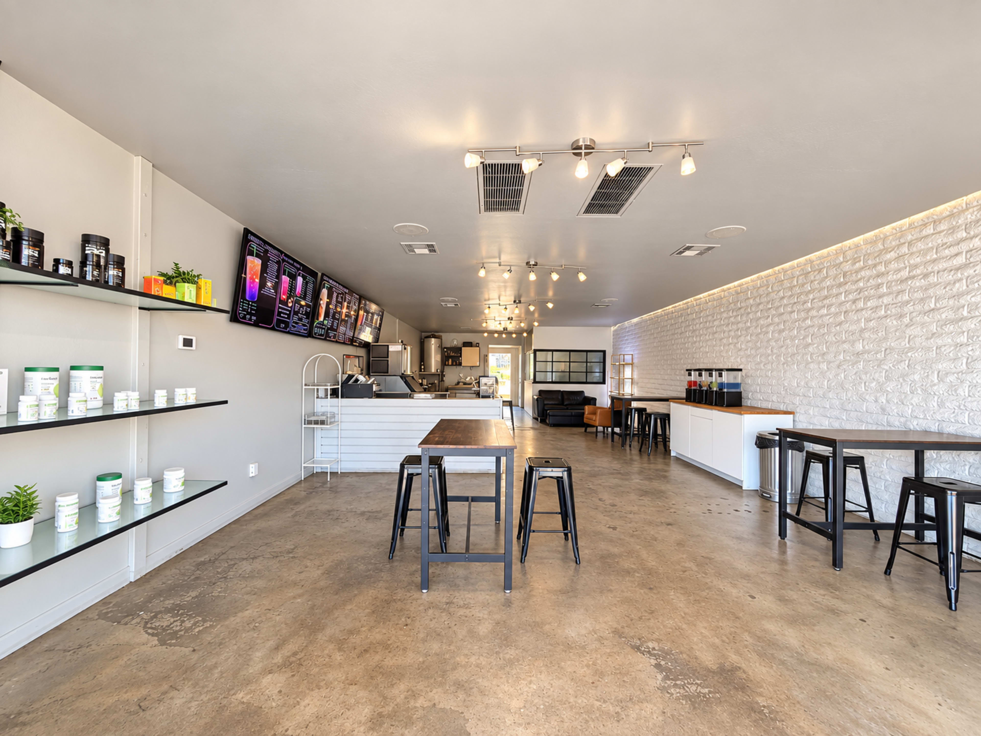 The image depicts a modern café interior featuring concrete floors, minimalist furniture, and shelves displaying various products.