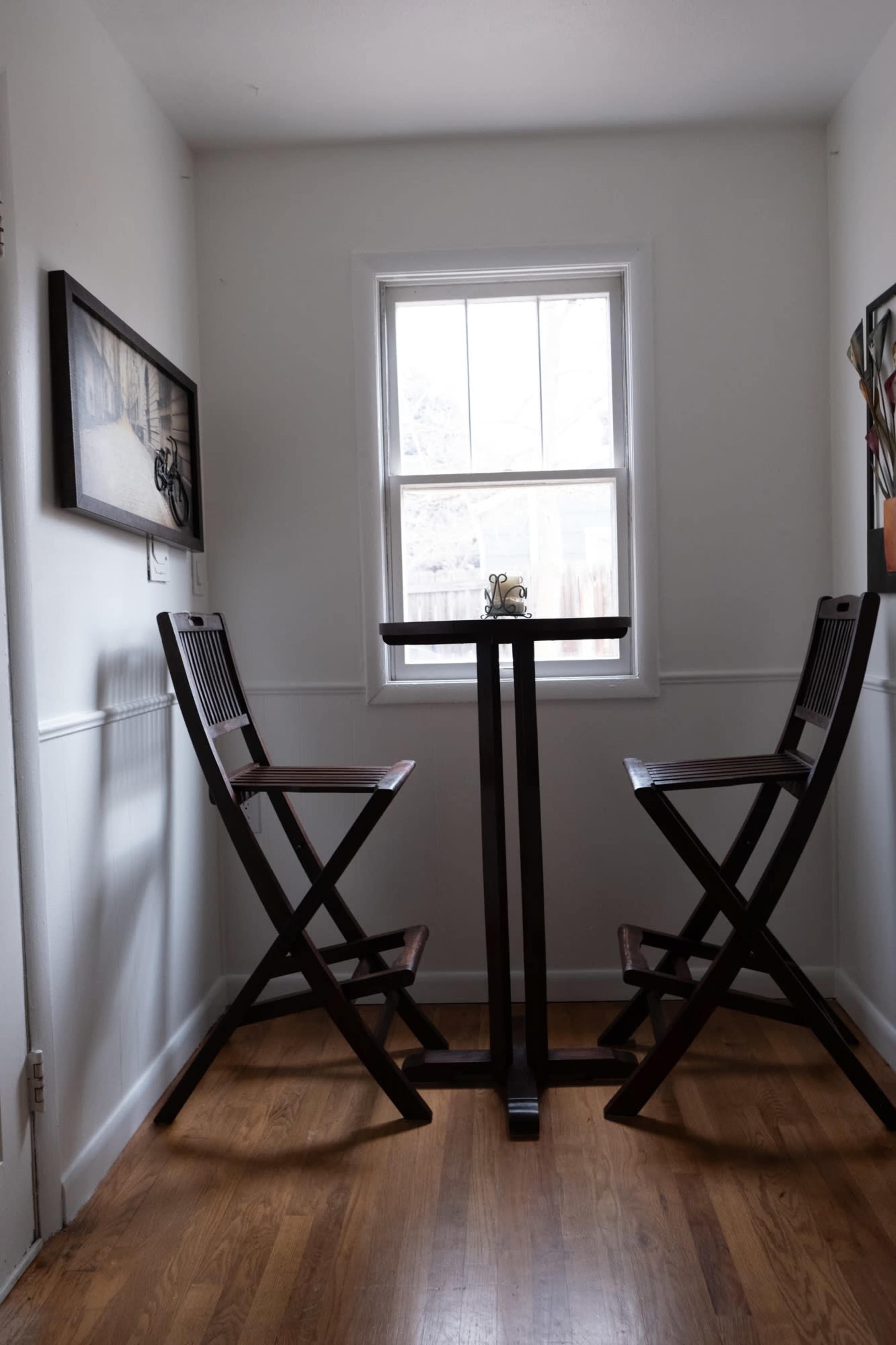 A small dining nook features two tall wooden chairs and a square table next to a window with natural light.