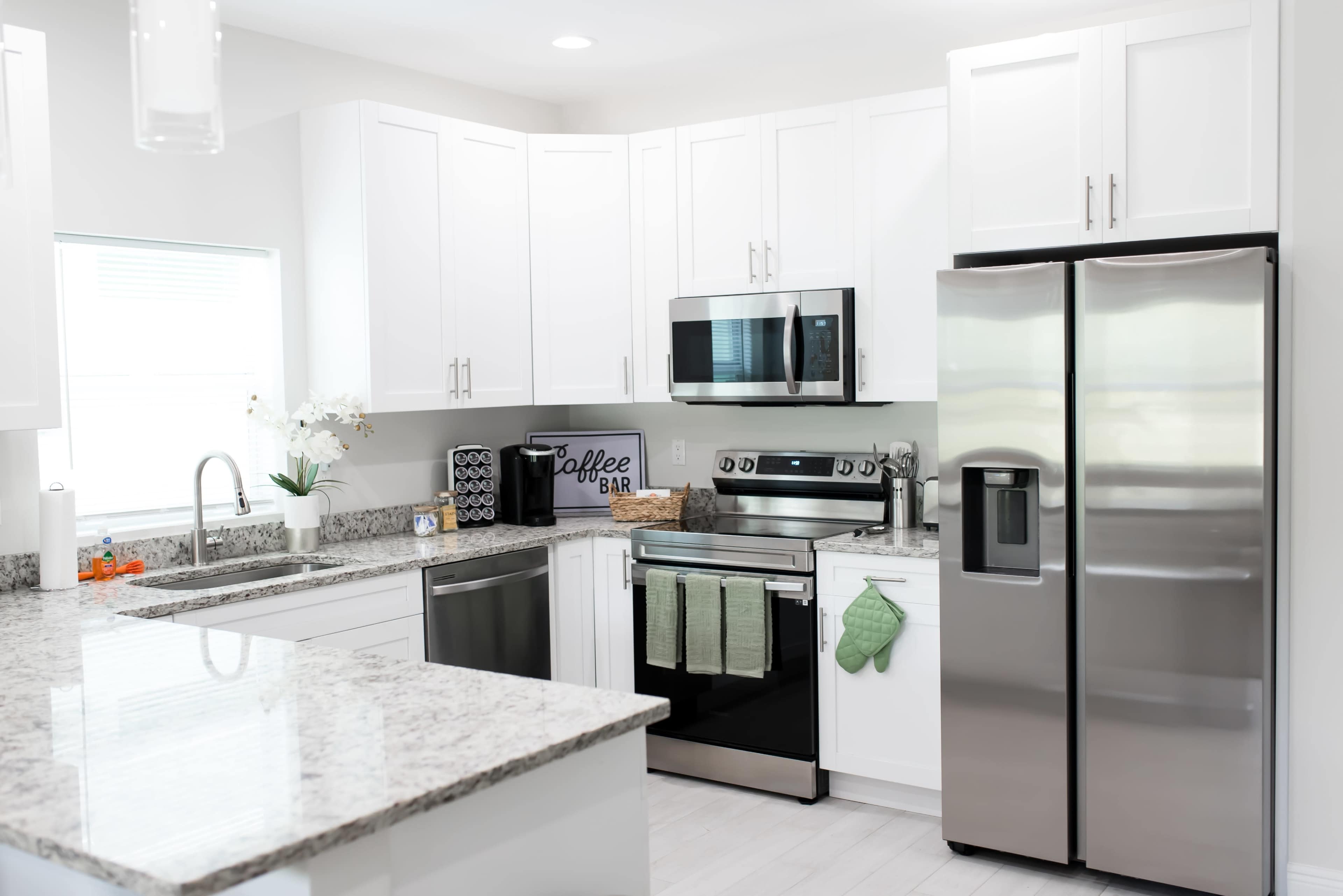 A modern kitchen features white cabinets, stainless steel appliances, and a granite countertop with a sink and decorative items.