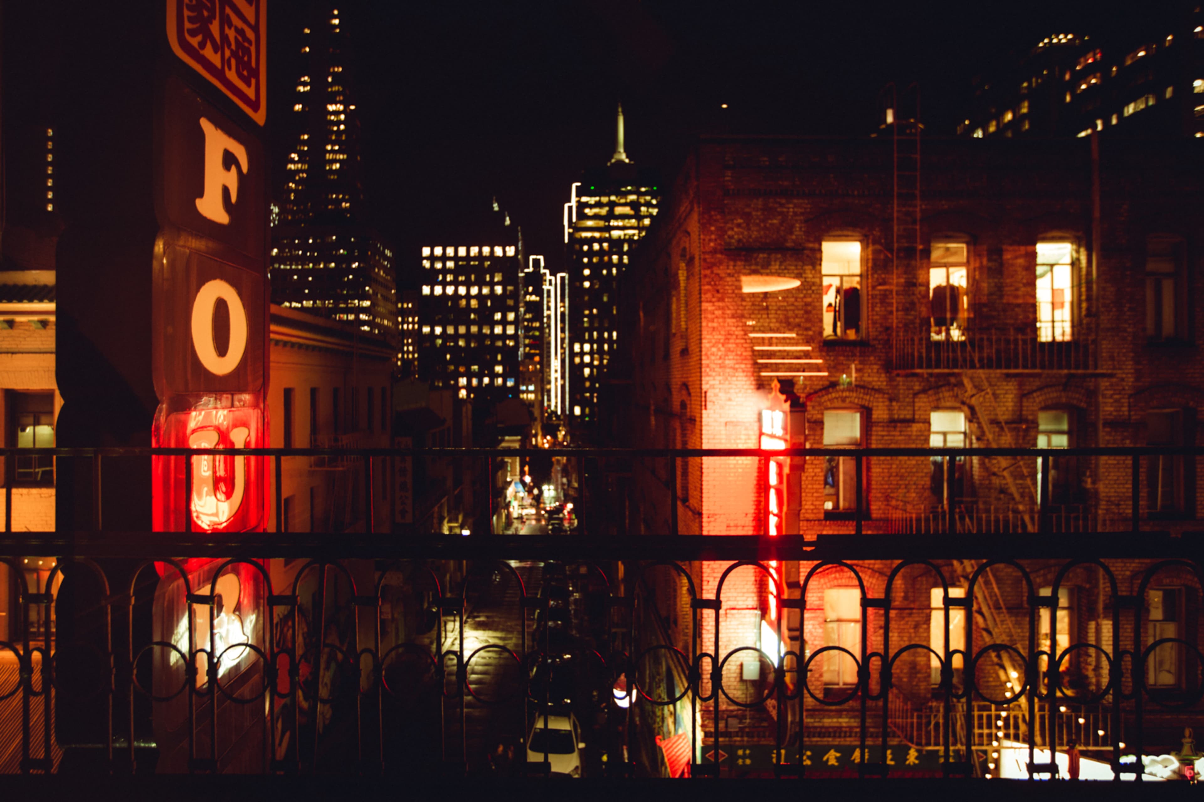 A nighttime cityscape features illuminated buildings and neon signs, with a view down a narrow street.
