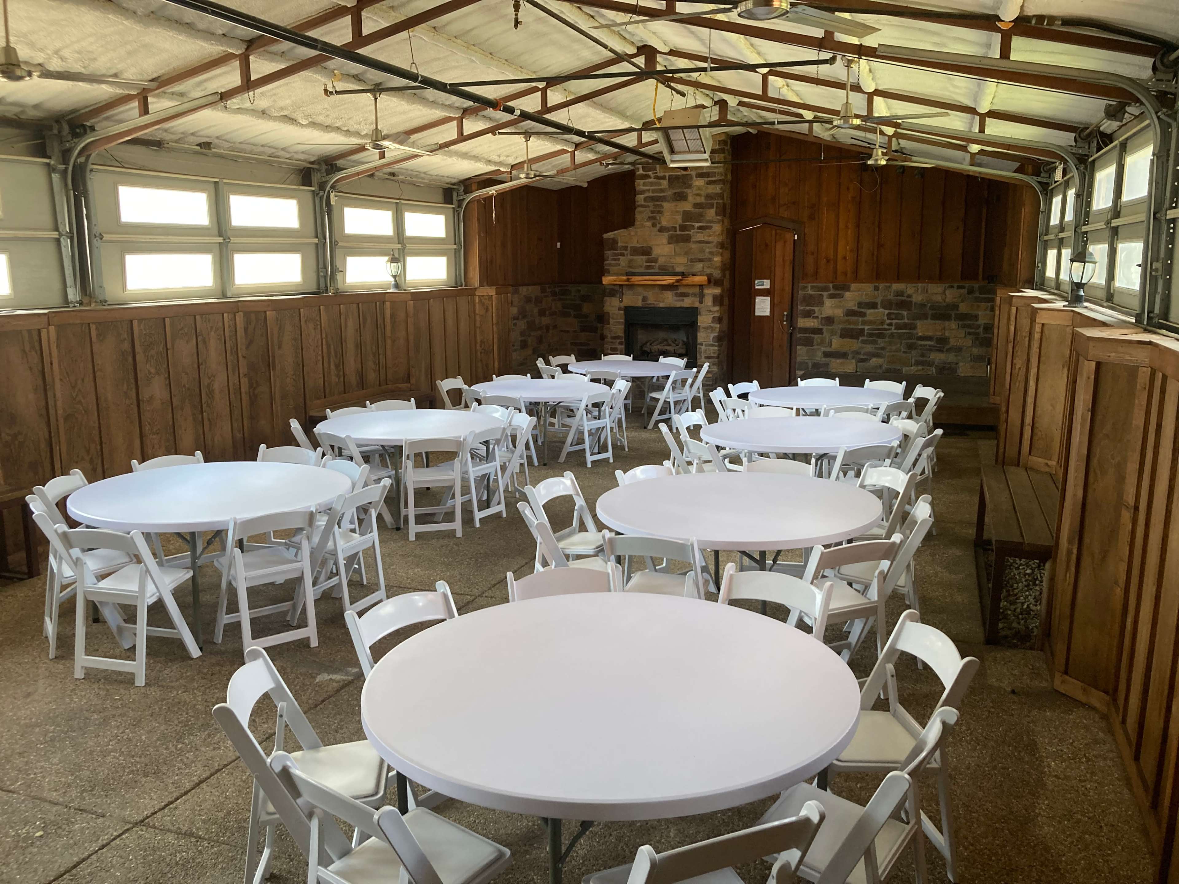 A spacious indoor gathering area with several round tables and white folding chairs arranged neatly throughout the room.