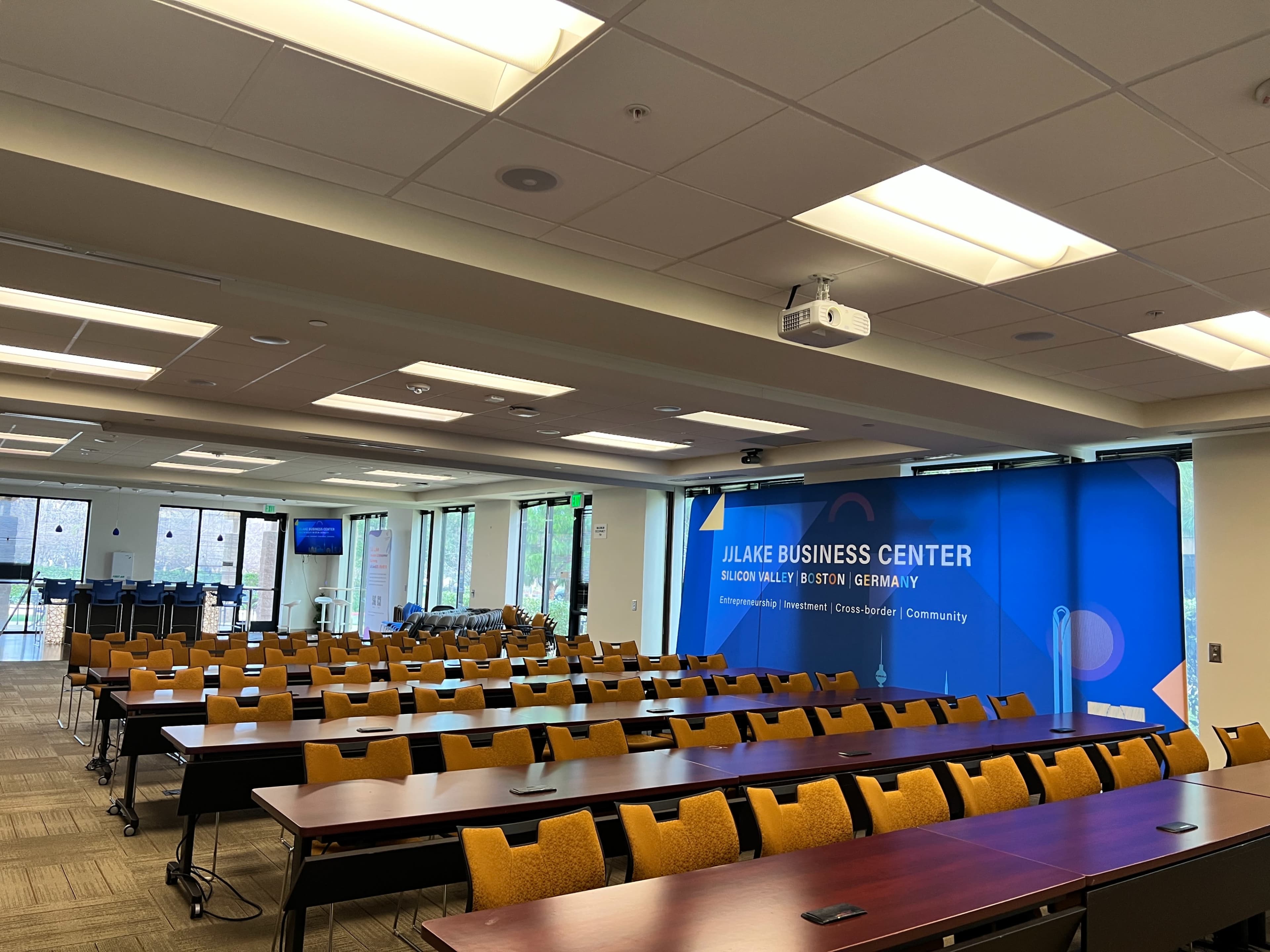 A spacious conference room with rows of tables and chairs, featuring a large blue banner for the Jilake Business Center along one wall.