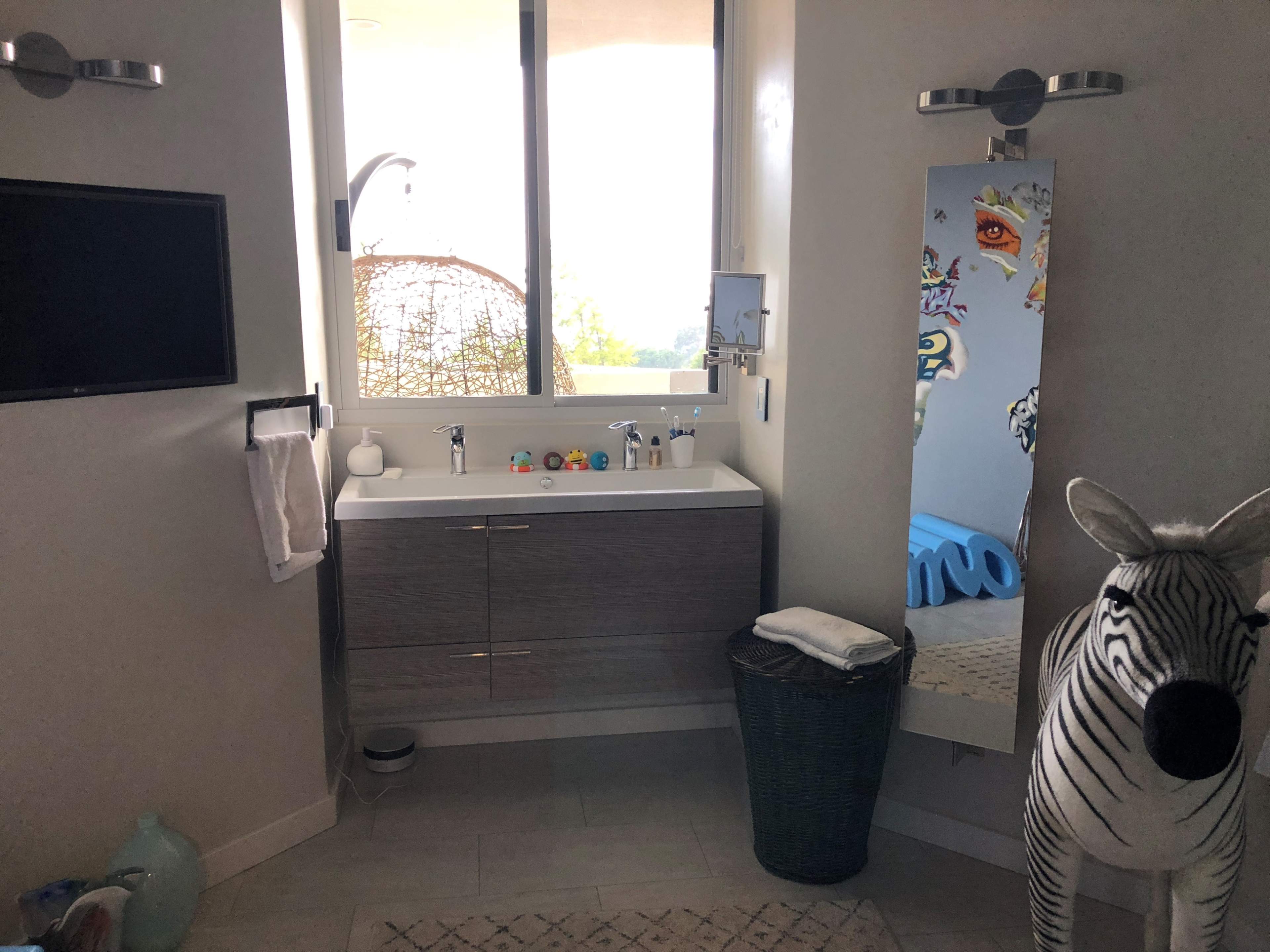 A modern bathroom featuring a large mirror, a sink with a vanity, a decorative zebra statue, and a hanging chair visible through a window.