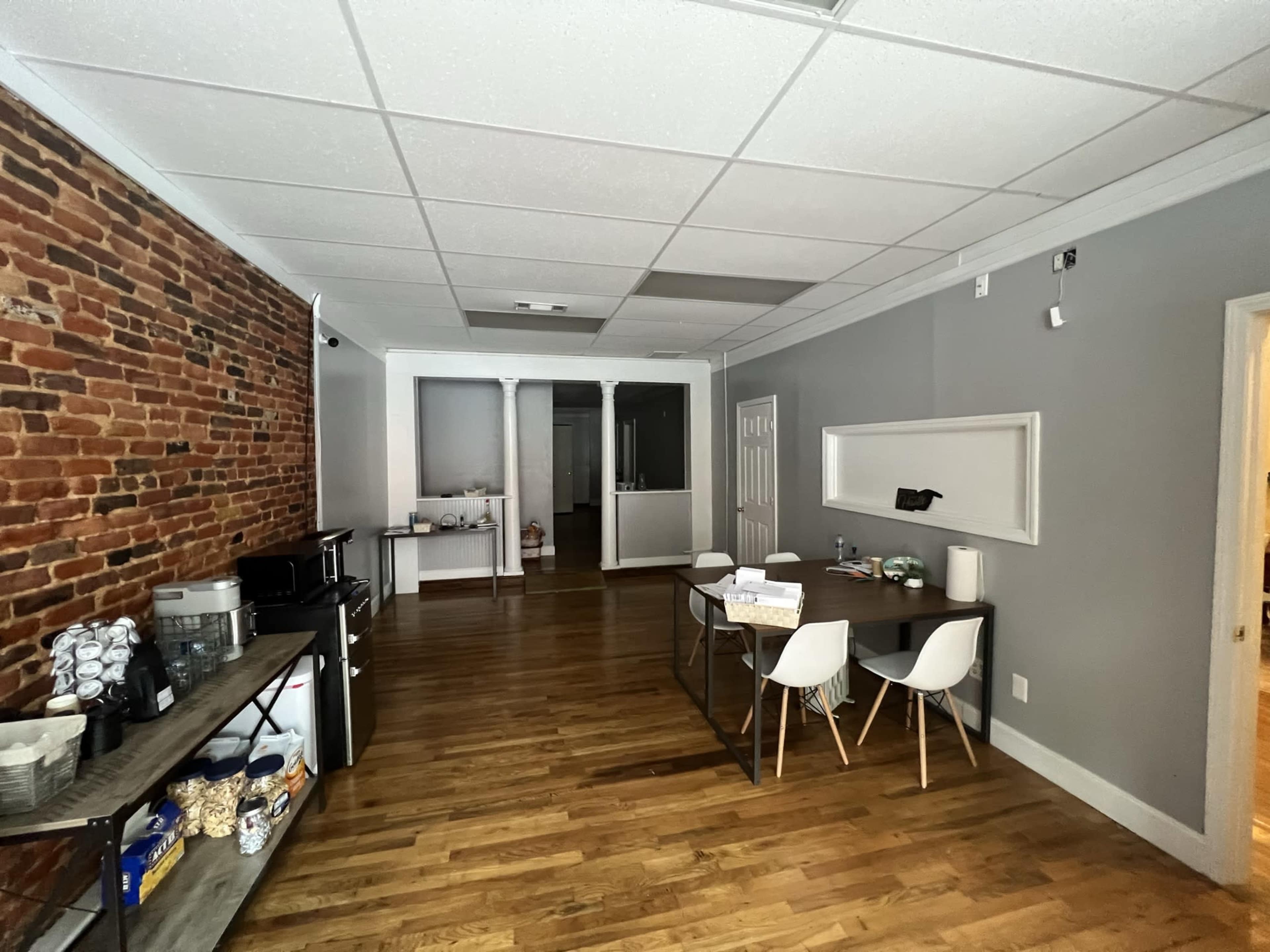 A spacious office with exposed brick on one wall, a dining table with chairs, and wooden flooring.