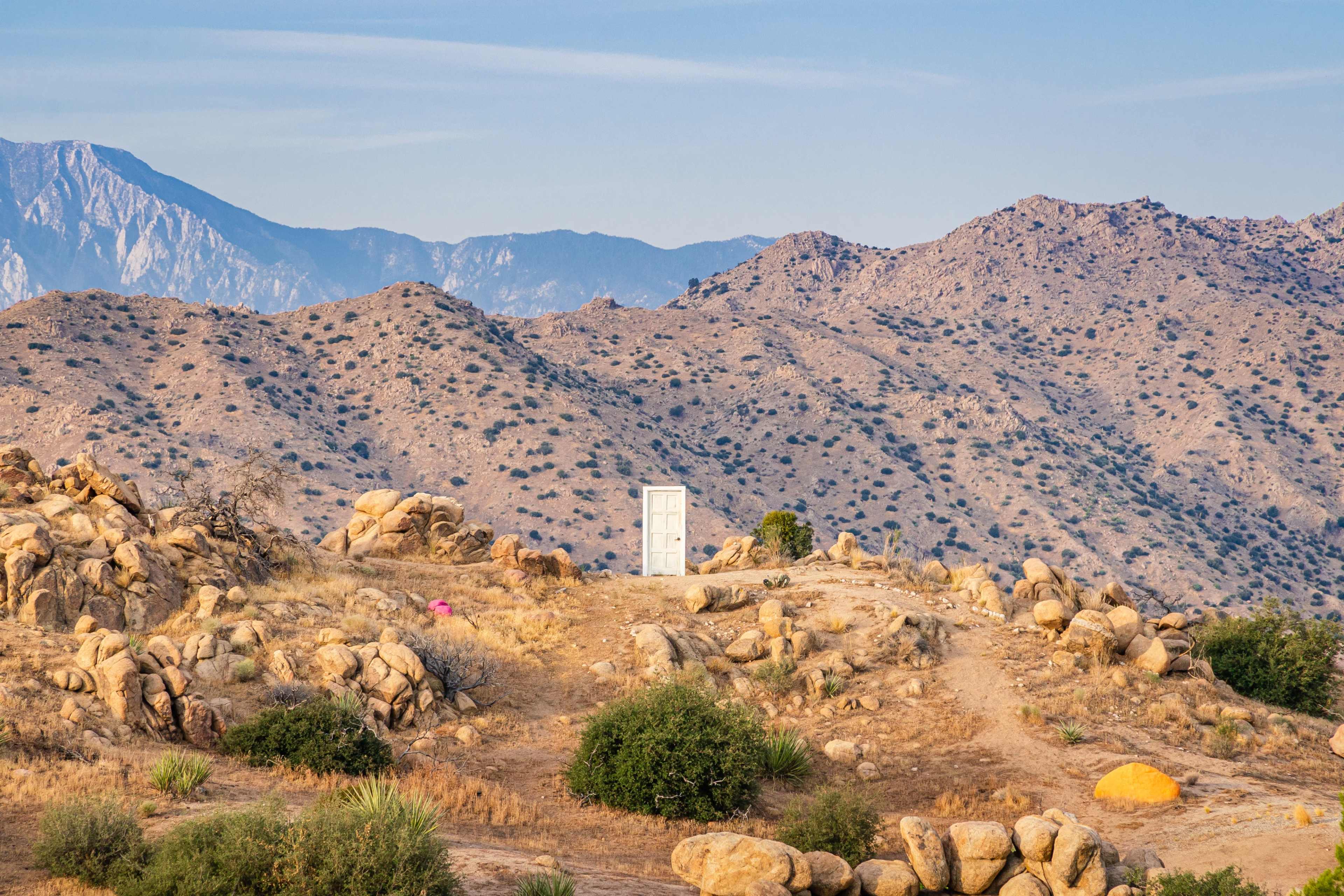 A solitary white door stands on a rocky hill amid a mountainous landscape.