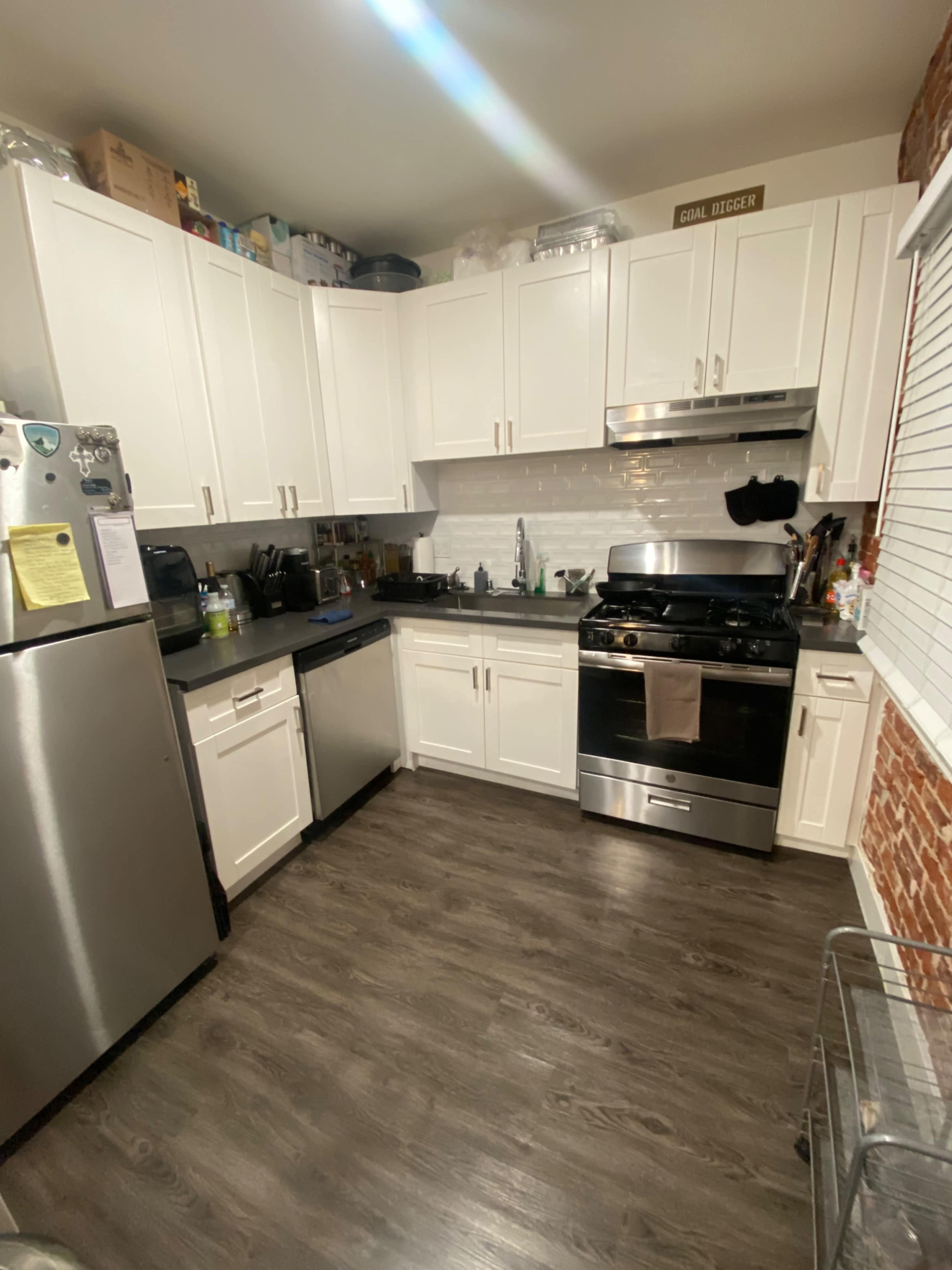 A modern kitchen features white cabinets, a stainless steel refrigerator and stove, and a wooden floor.