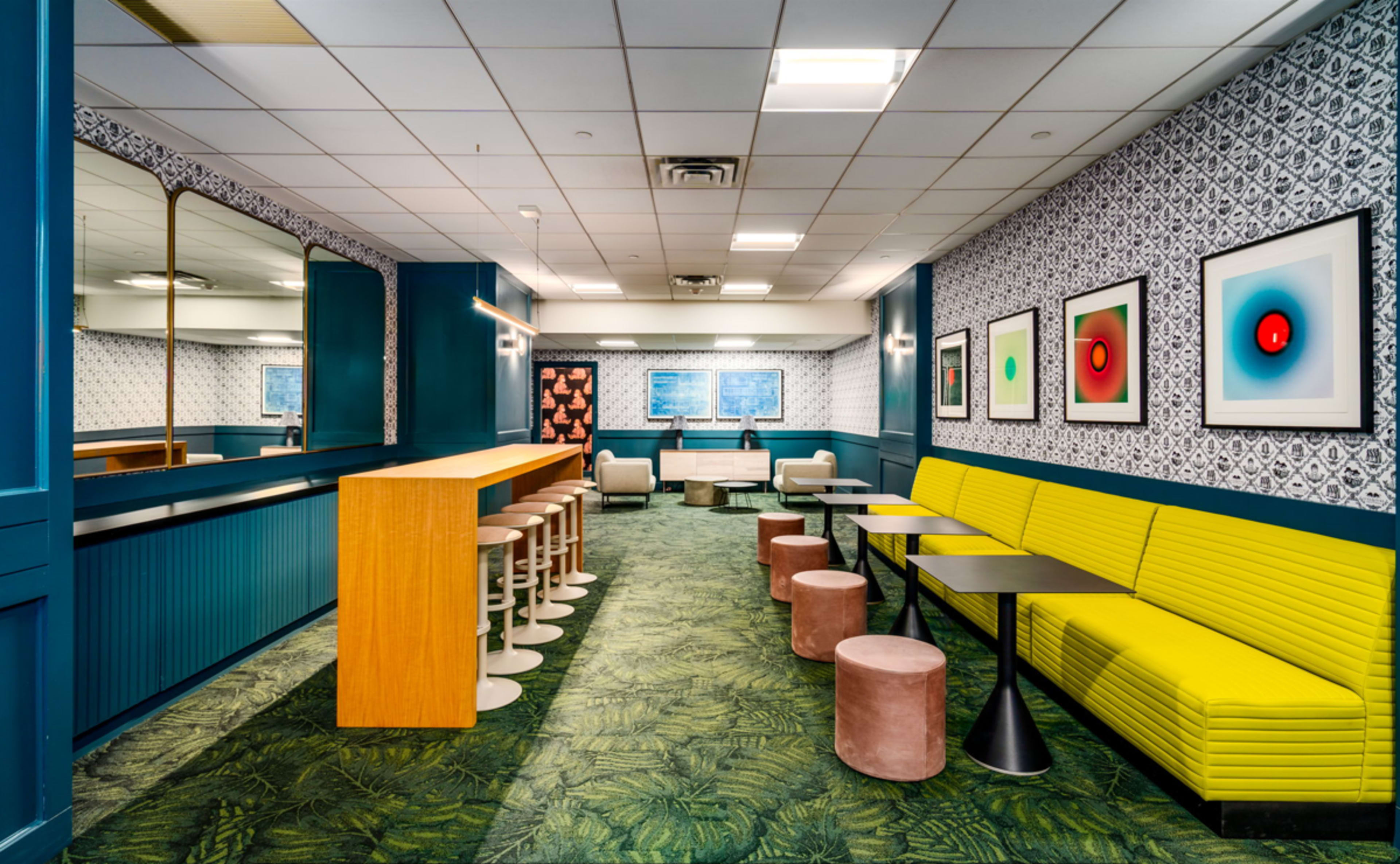 A modern lounge area featuring yellow seating, wooden bar counters, and vibrant artwork on the walls.